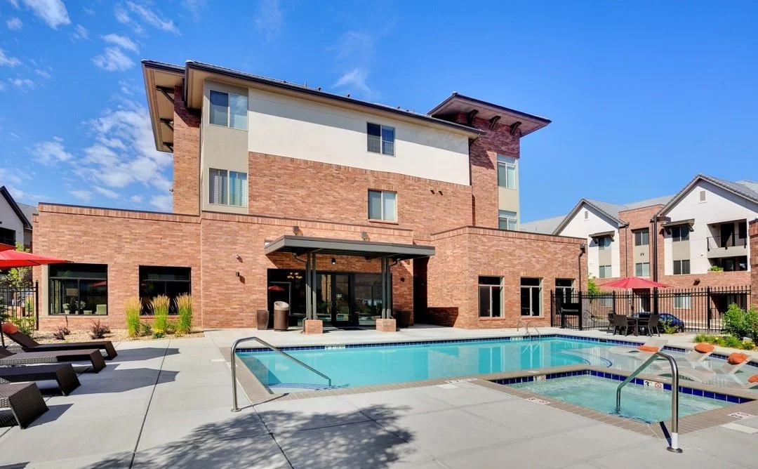 Apartment complex with a swimming pool, hot tub, and lounge chairs, located outdoors on a sunny day.