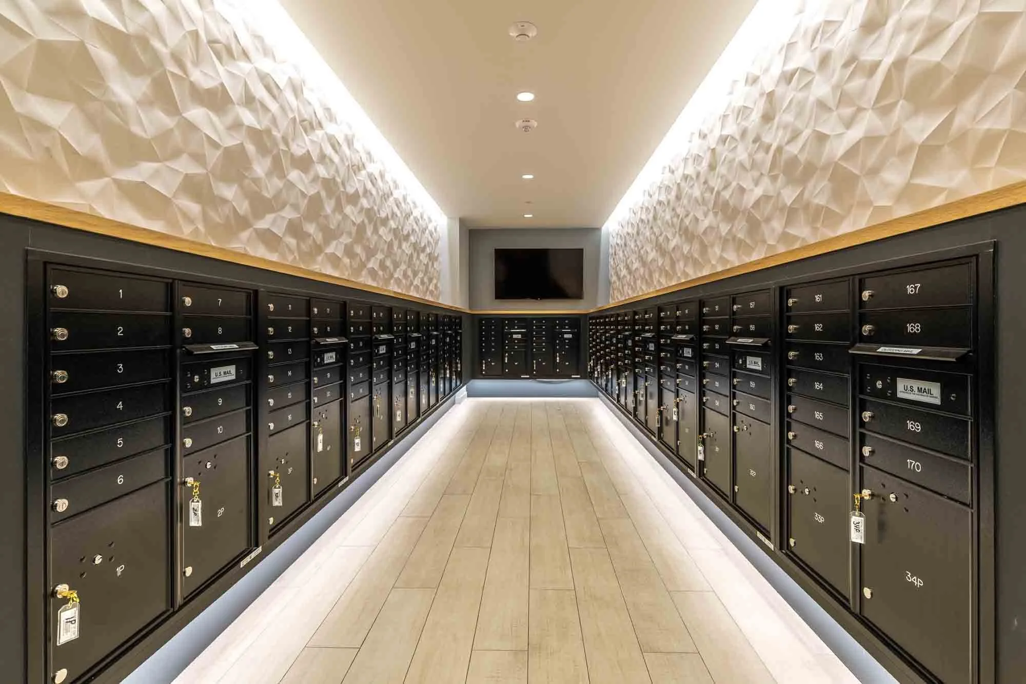 Indoor mailroom with black mailboxes, a wall-mounted television, and modern textured wall panels
