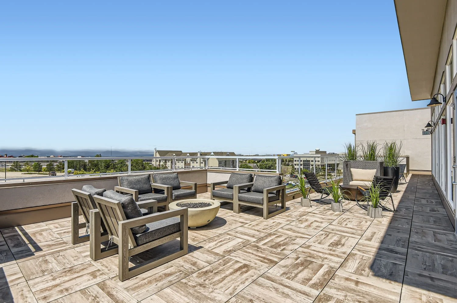 City view from a rooftop terrace with outdoor seating, including cushioned chairs, a fire pit, and potted plants.
