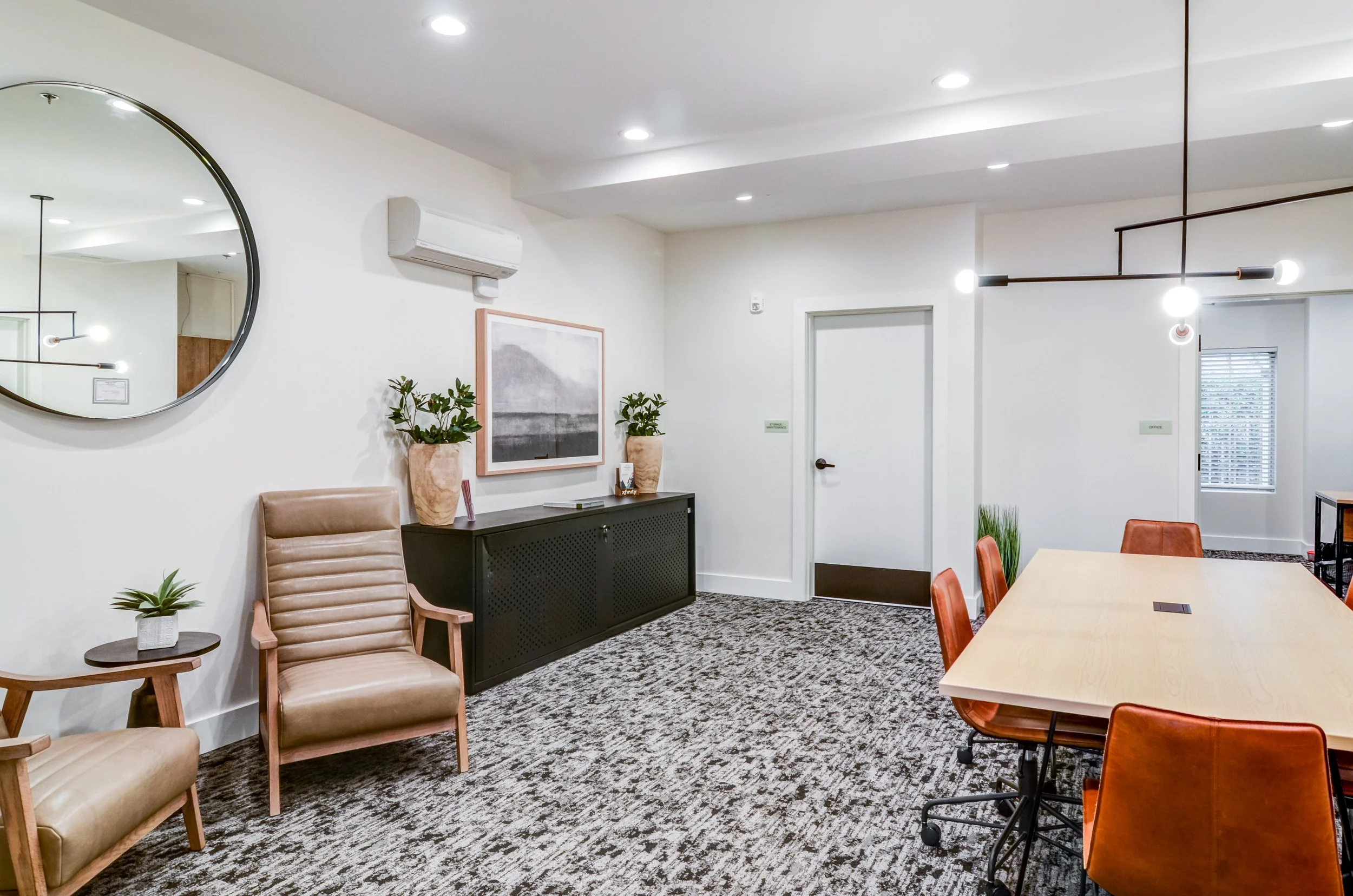 Modern conference or meeting room with chairs around a table, wall decor, potted plants, and contemporary lighting fixtures.