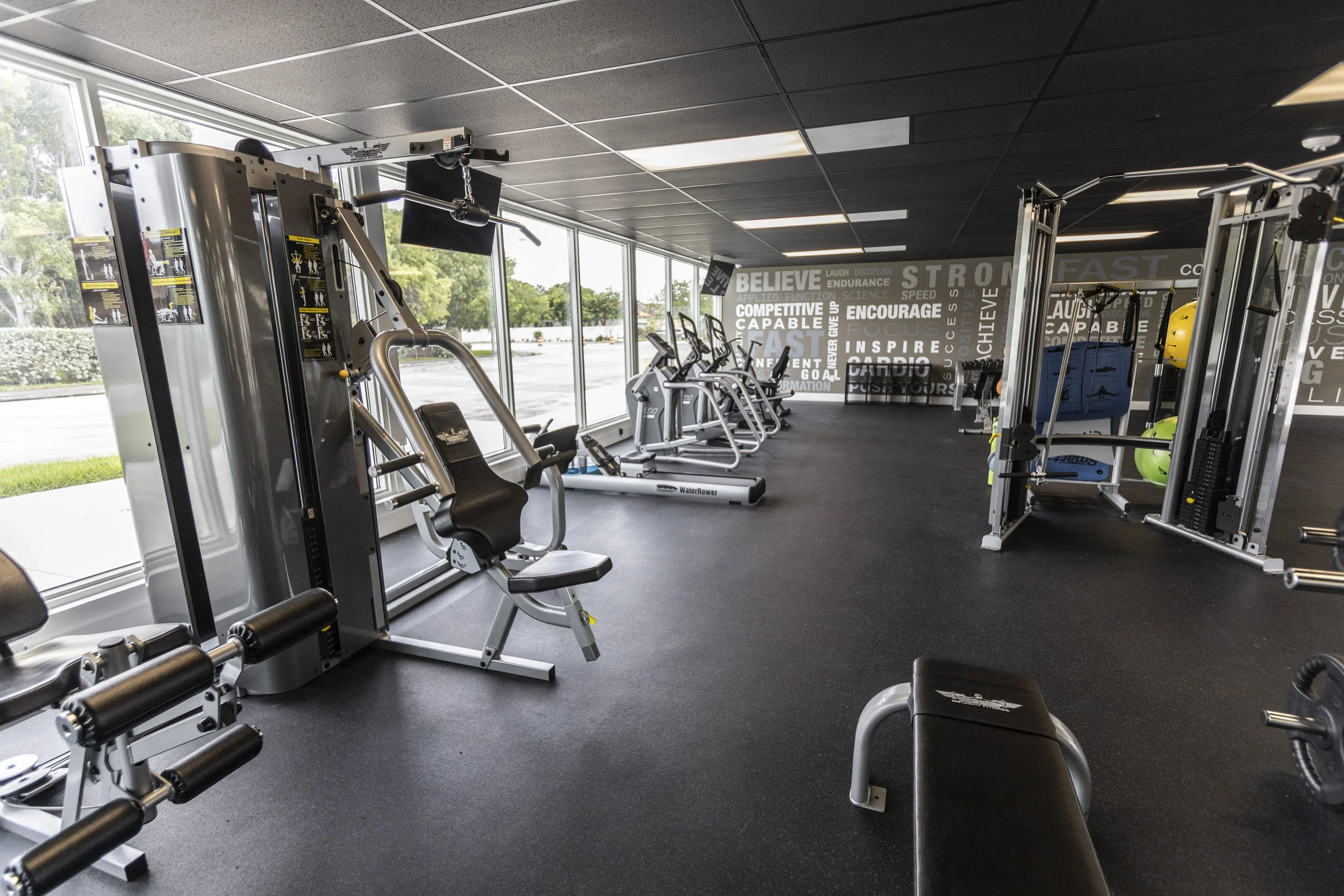 Interior view of a gym with exercise machines, weights, and motivational wall graphics.