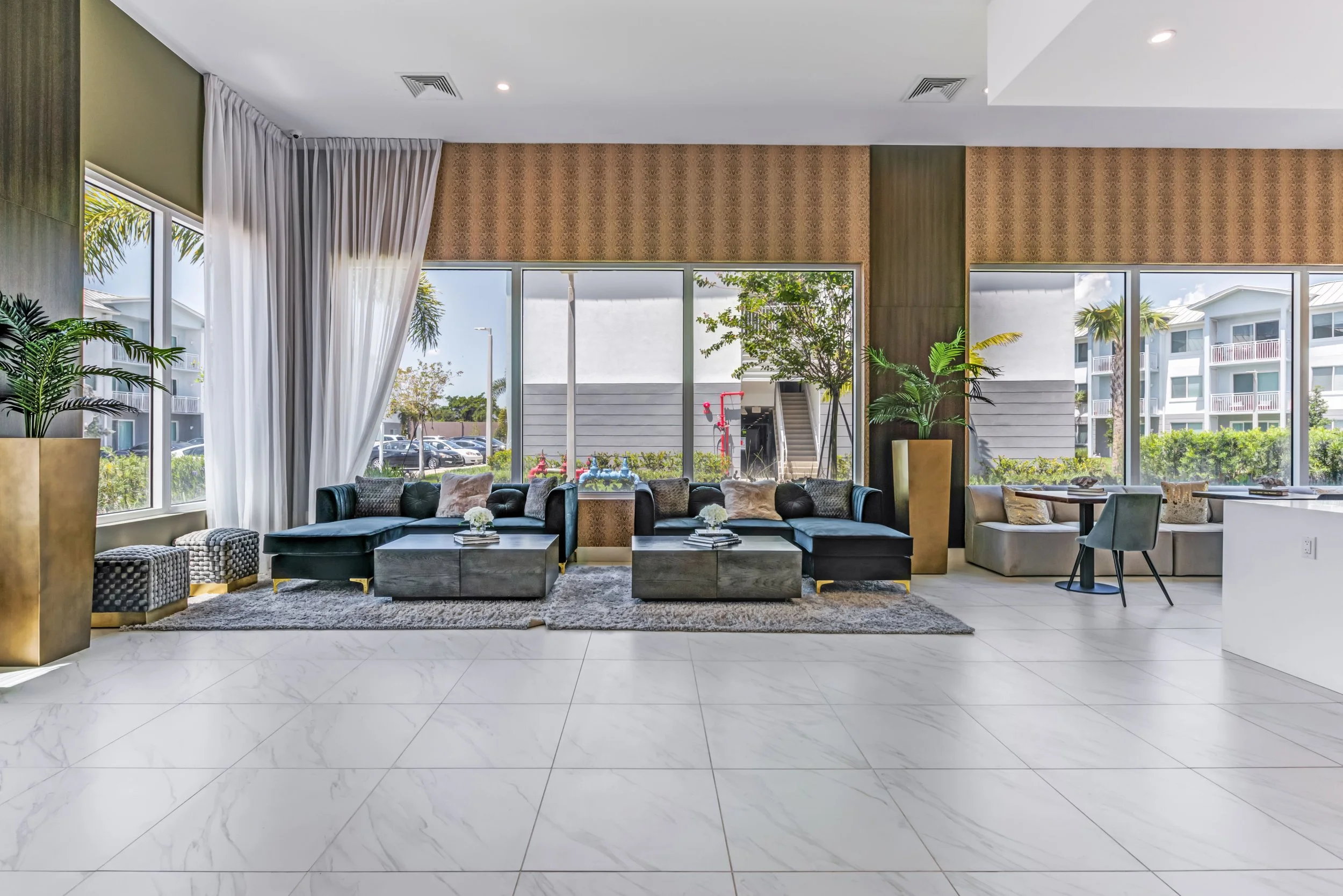Modern hotel lobby with large windows, black sofas, and potted plants, decorated in neutral tones.