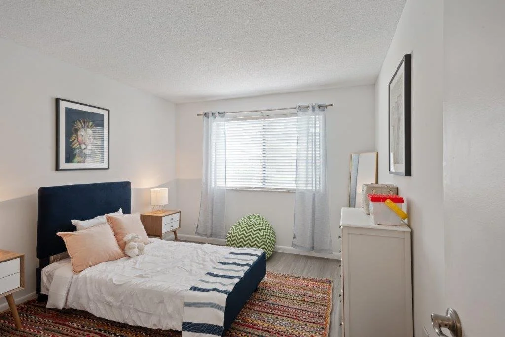 A bedroom with a bed, nightstands, and a window with blinds and light curtains.