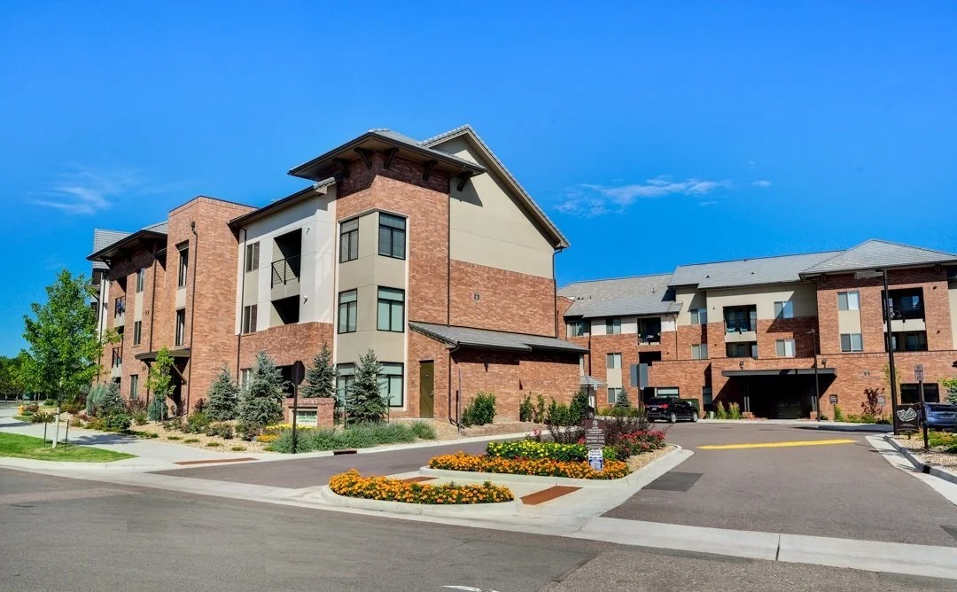 Modern apartment complex with brick and stucco exterior, landscaped surroundings, and clear blue sky.