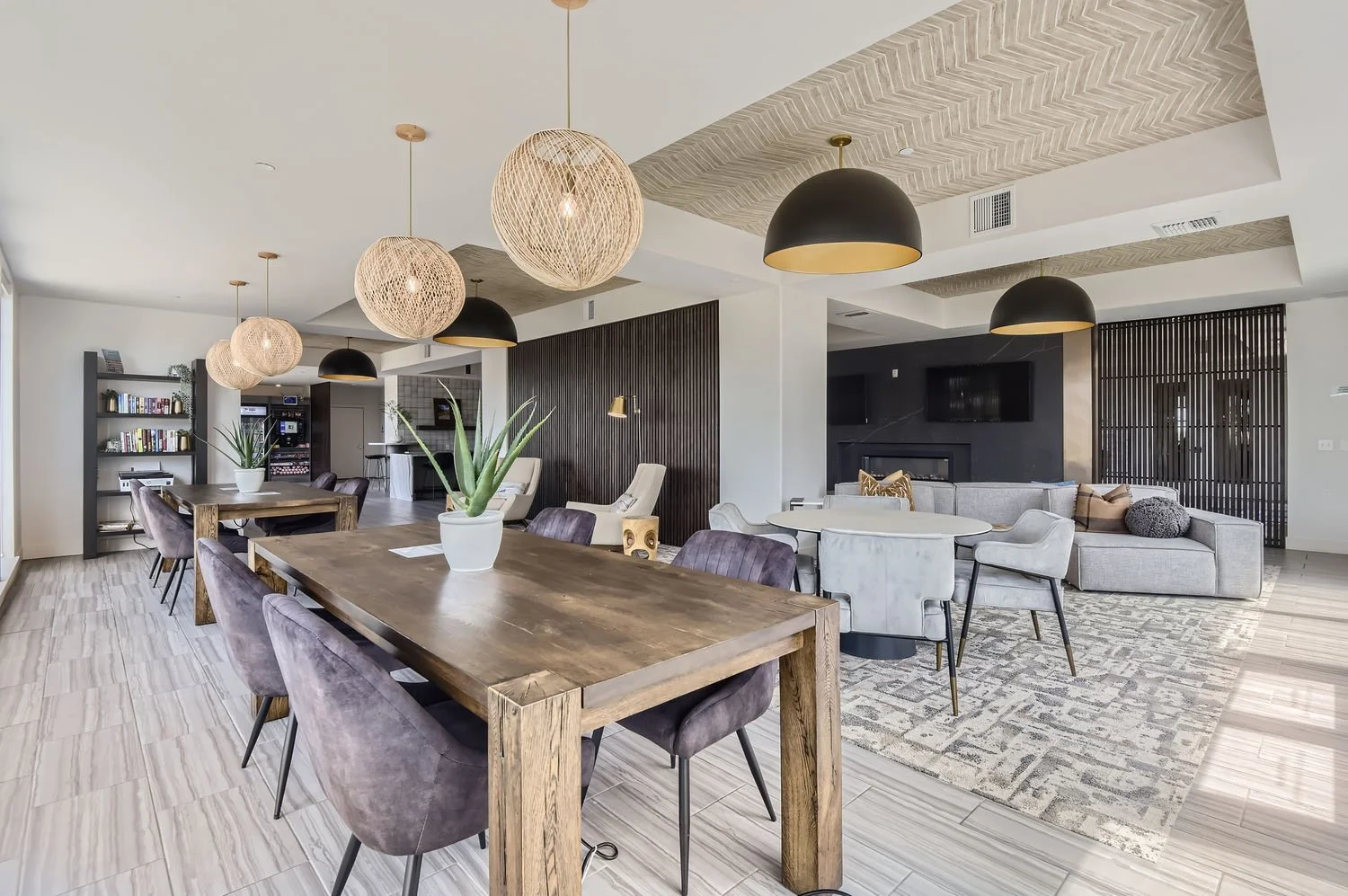 Modern open-concept living and dining room with wooden dining table, purple velvet chairs, white and beige seating area, pendant lights, gray rug, dark wood accents, and recreational area.
