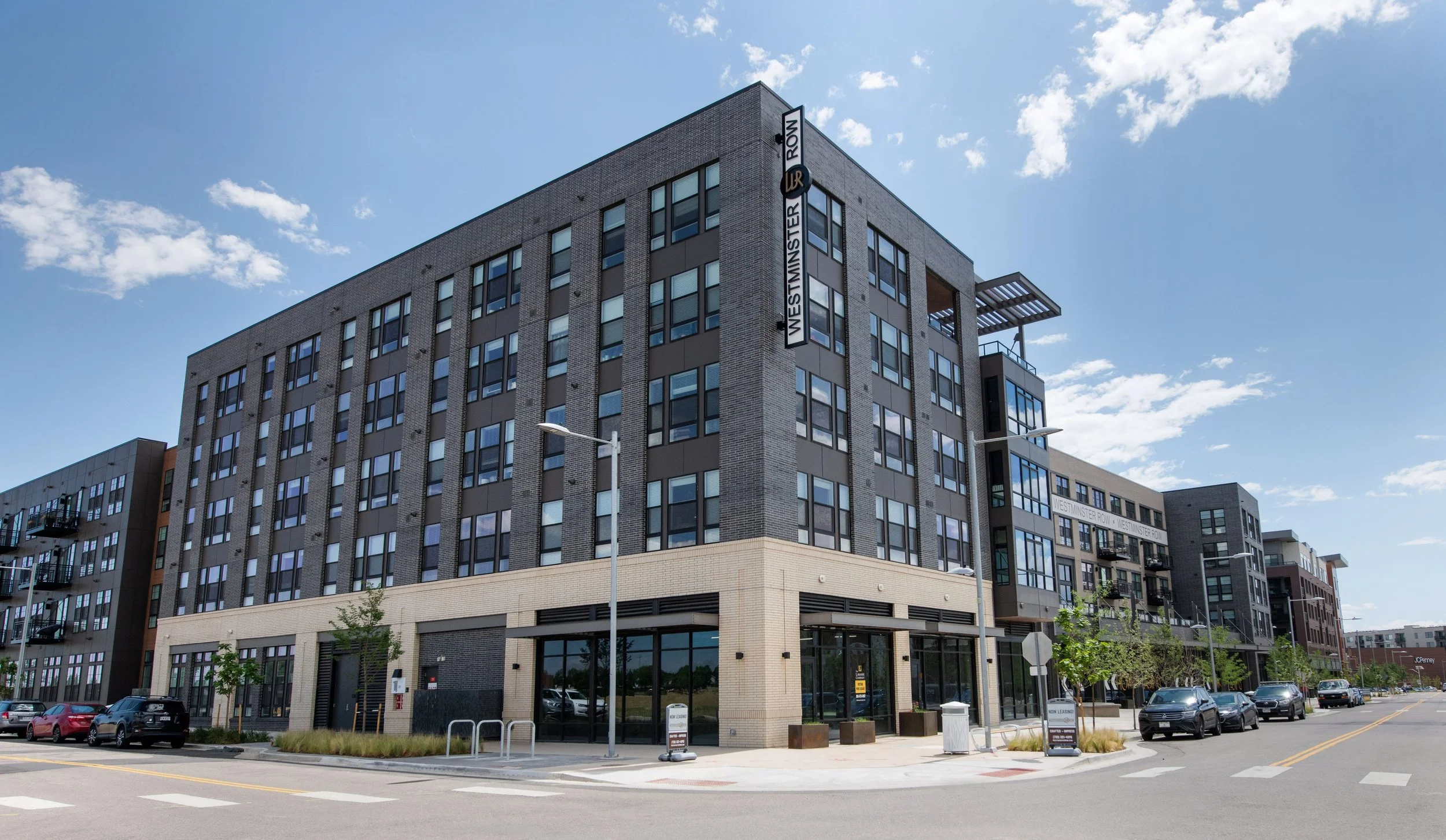 Modern multi-story apartment building on Westminster Row with large windows, street parking, and a clear blue sky.