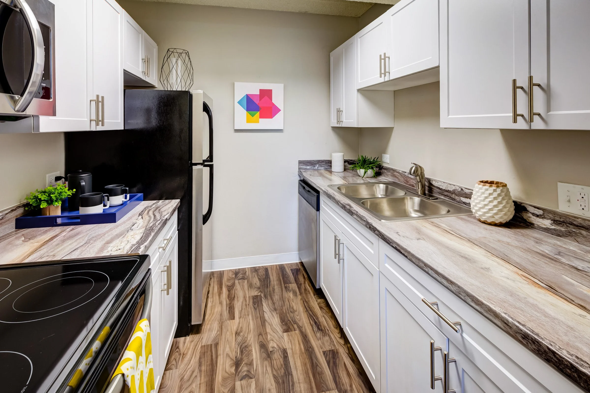 Modern kitchen with white cabinets, marble countertop, stainless steel double sink, black refrigerator, stove, and decorative items like a potted plant, a vase, and a painting on the wall.