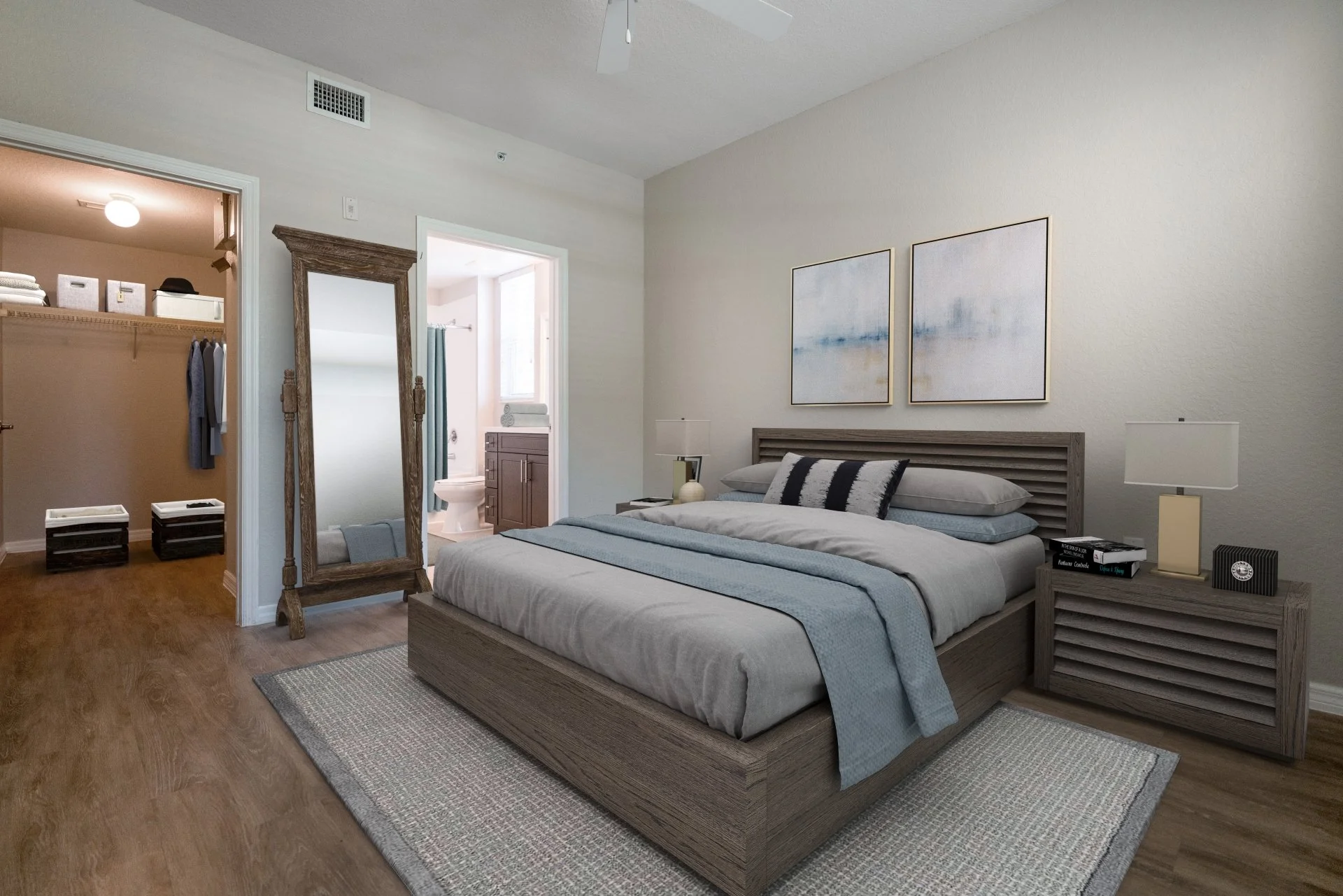 A modern bedroom with a wooden bed frame, gray bedding, and blue accents. Two abstract art pieces hang above the bed. A small wooden nightstand with books and a lamp is on one side of the bed. An open doorway reveals a bathroom and walk-in closet wit