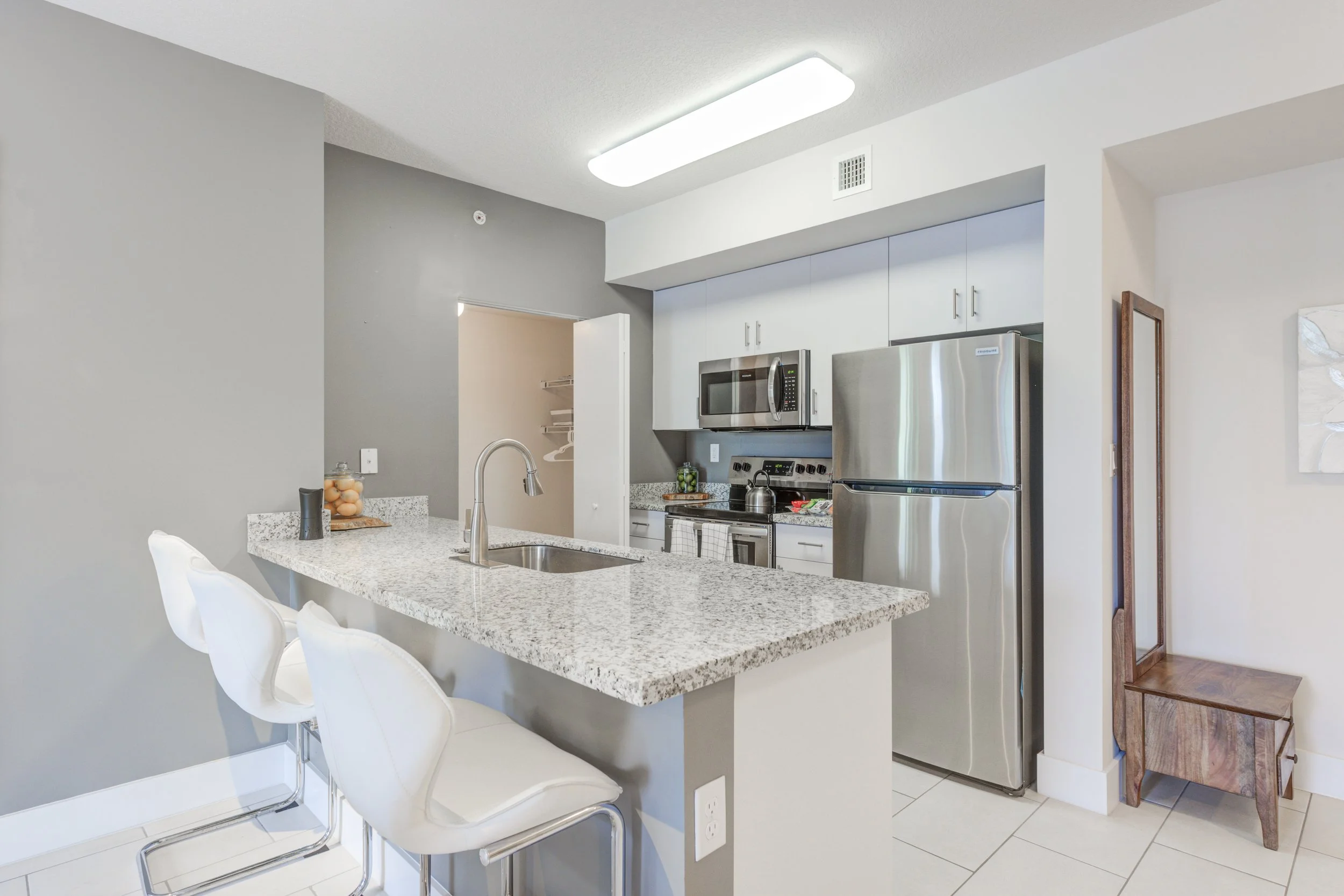 Modern kitchen with granite countertop, stainless steel fridge, microwave, stove, and white cabinets