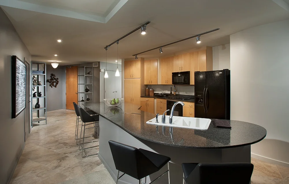 Modern kitchen with black countertop island, wooden cabinets, black appliances, bar seating, and track lighting.