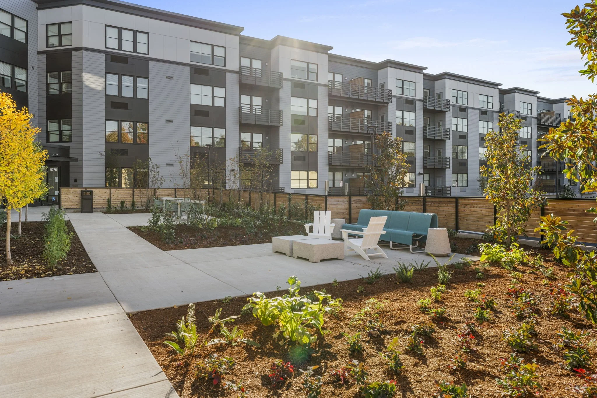 Outdoor patio area with seating and landscaping in front of modern apartment building during daytime.
