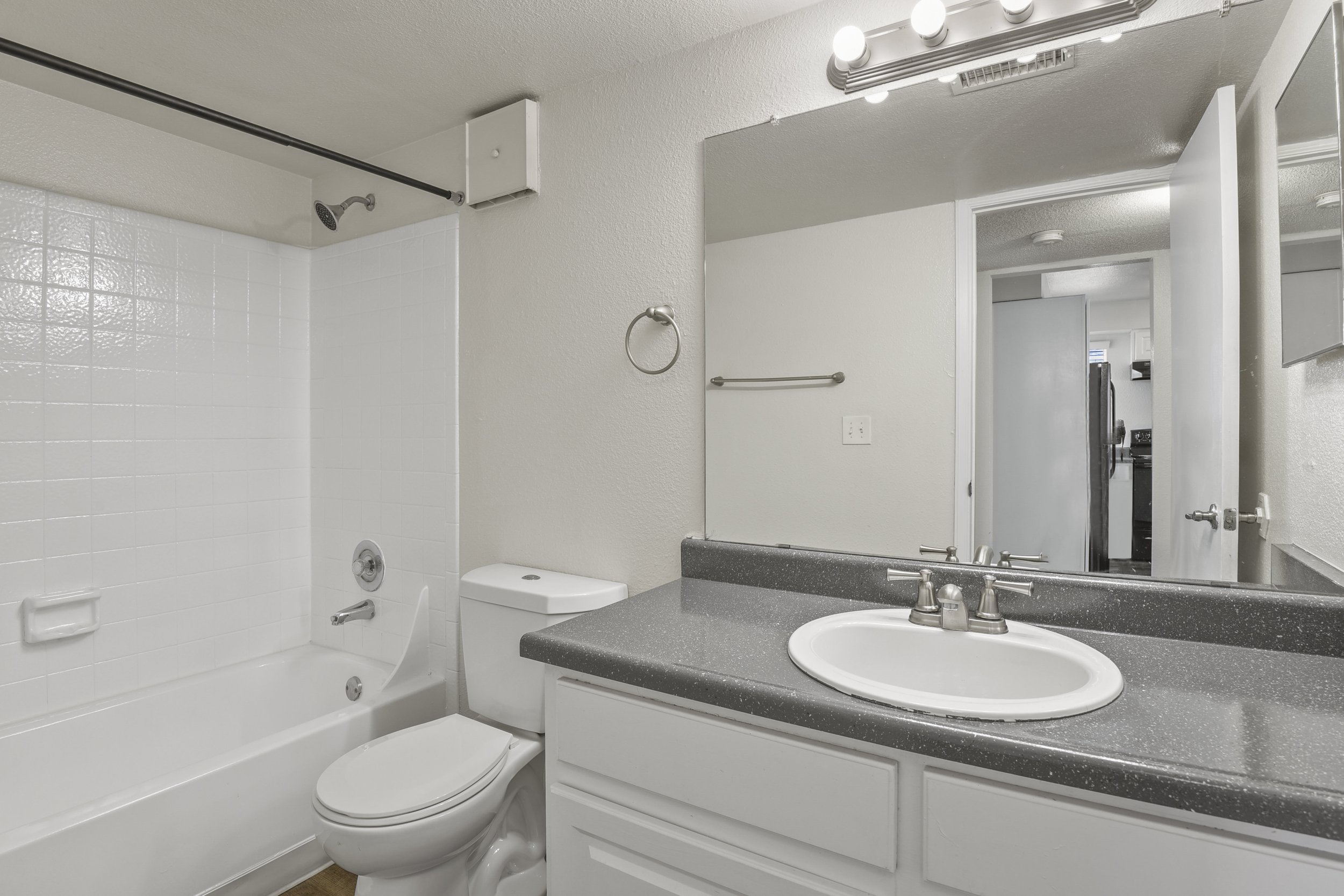 Bathroom with bathtub, toilet, mirror, and sink with grey countertop.