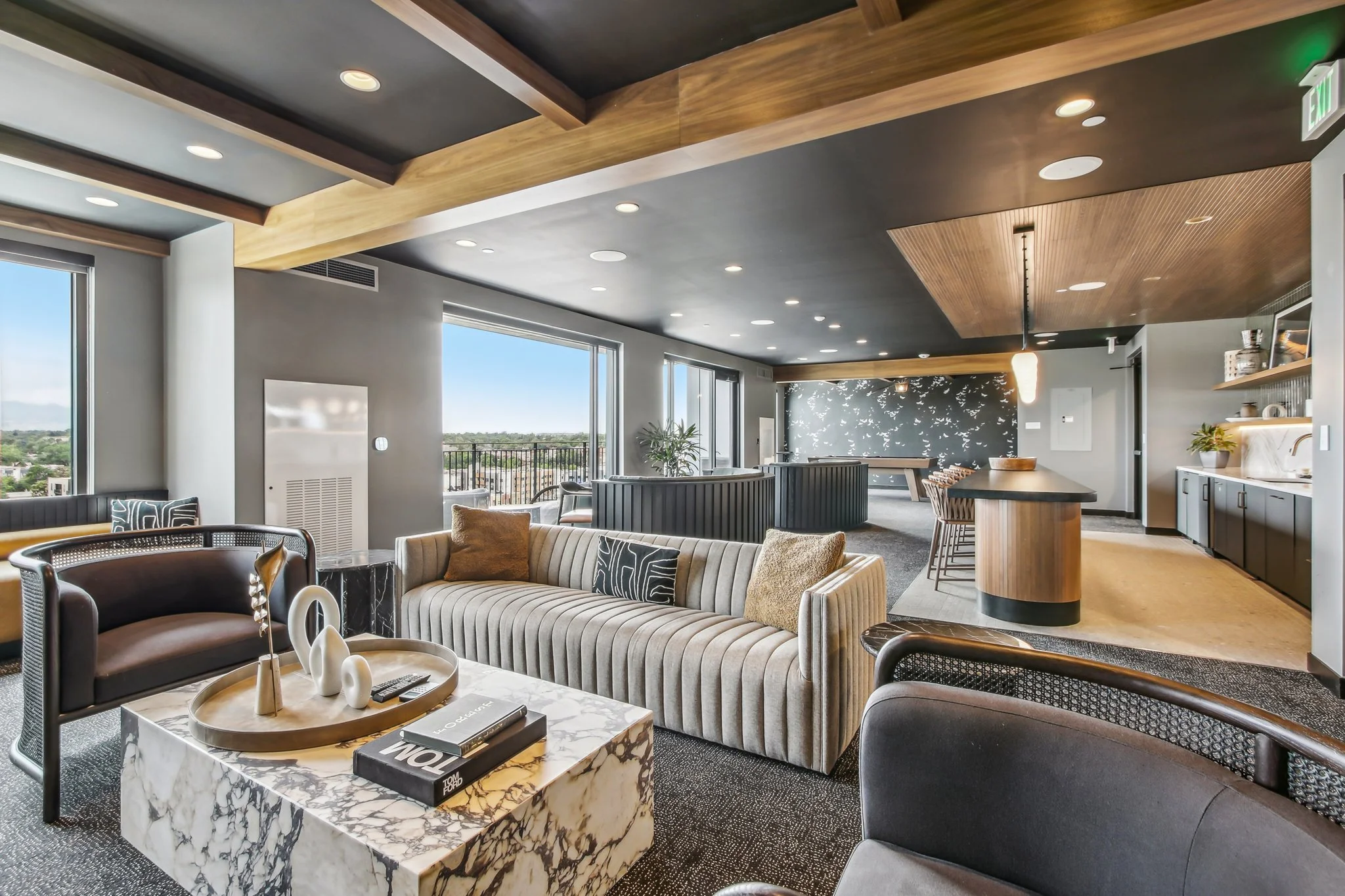 Modern living room with large windows, gray walls, wooden ceiling accents, a marble coffee table, striped sofa, and various chairs, opening to a balcony with a view.