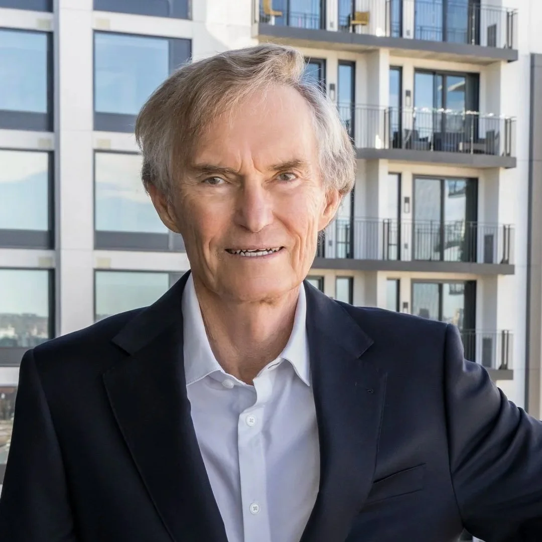 A middle-aged man with light brown hair, wearing a blue shirt, smiling slightly, indoors with a blurred background.