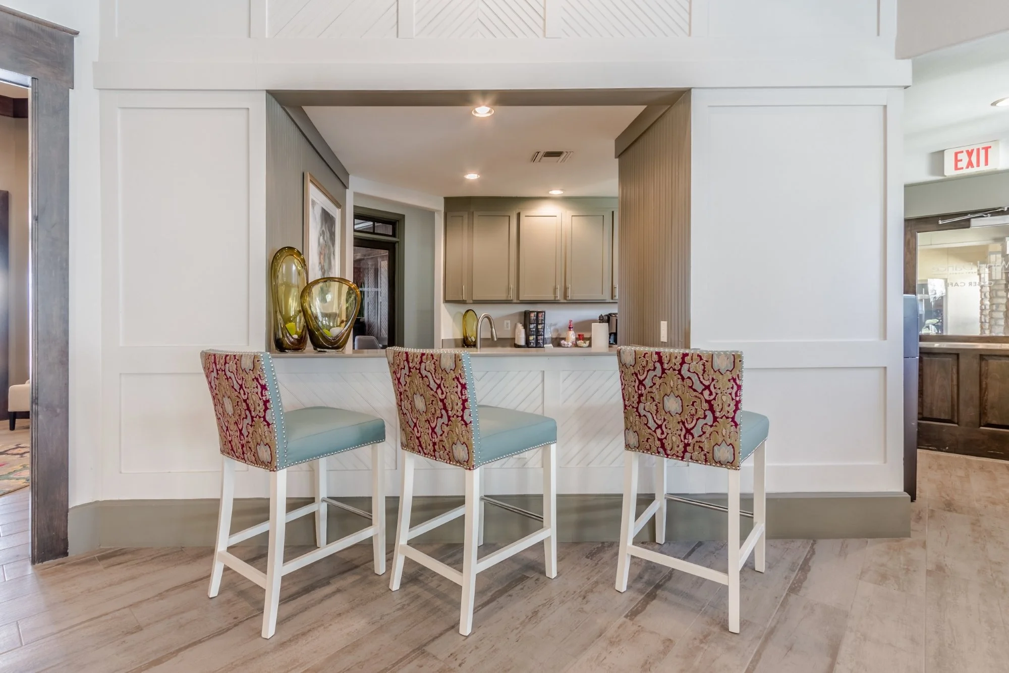 Three barstools with turquoise seats and patterned backs in front of a kitchen pass-through in a bright, modern room.