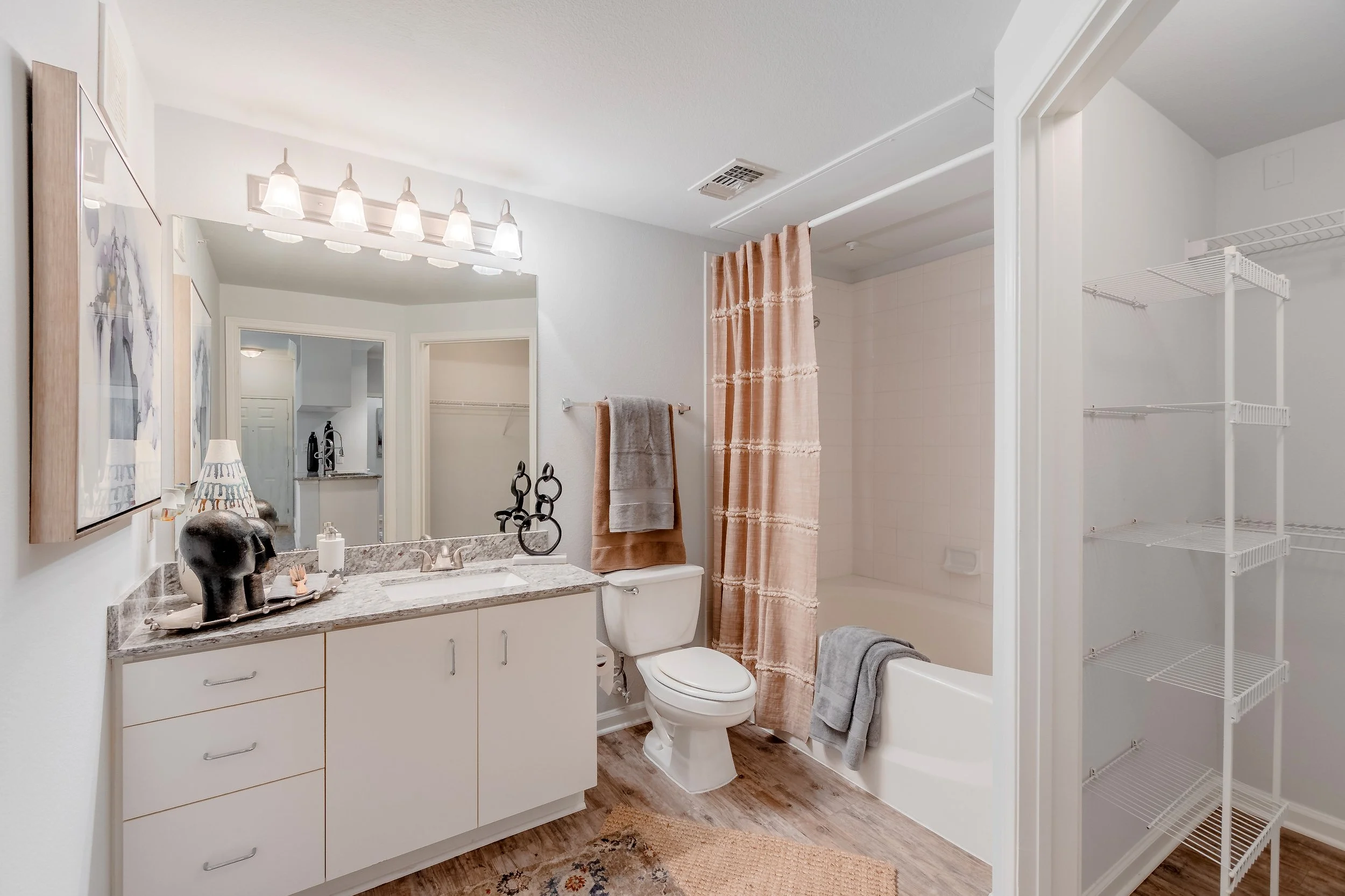 Bathroom with white vanity, granite countertop, decorative objects, two towels, a shower curtain, a bathtub, and an open shelving unit.