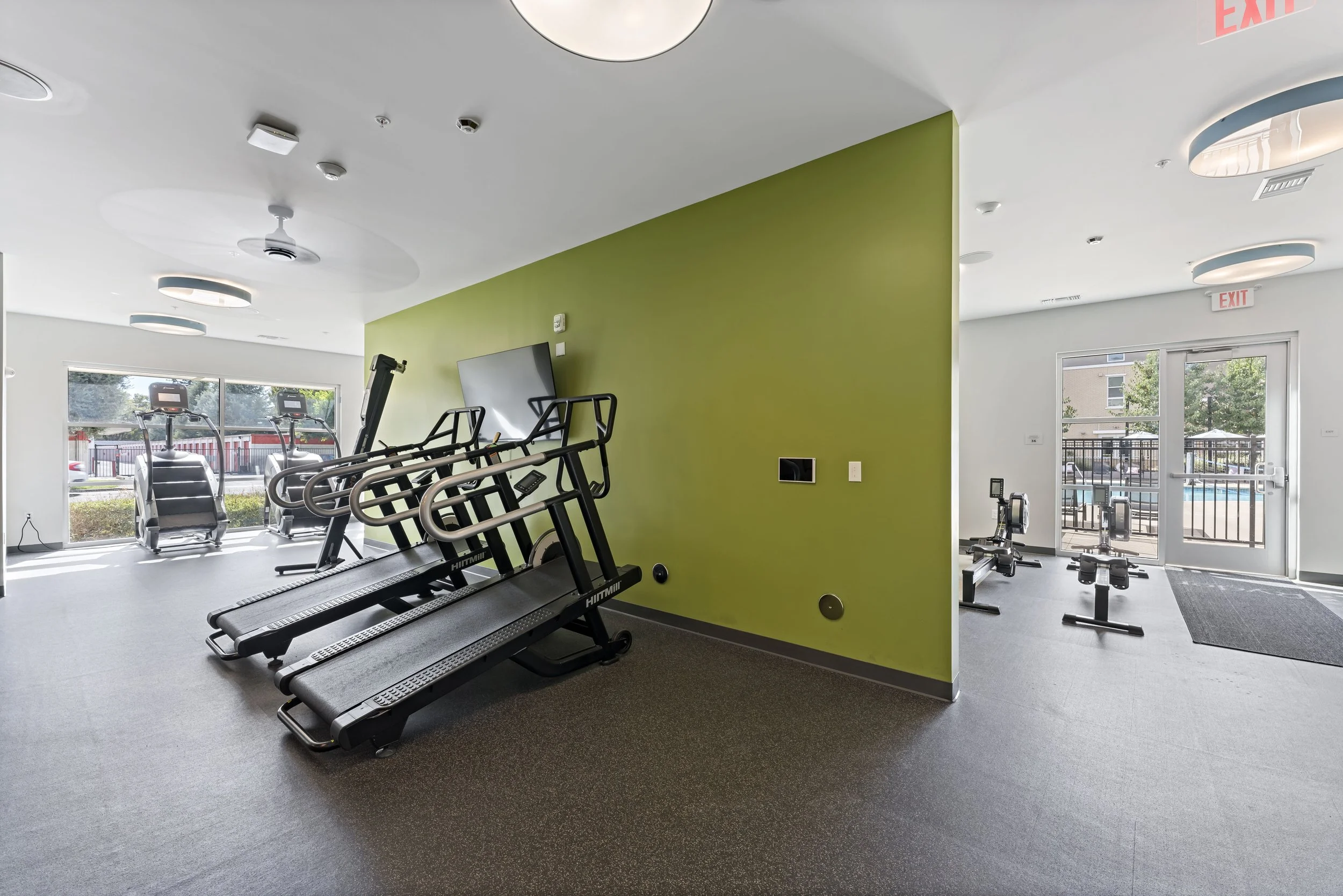 Fitness center with treadmills and exercise bikes, large windows, and a green accent wall.