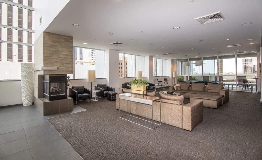 Spacious modern lounge with large windows, black armchairs, beige sectional sofa, fireplace, and city view.
