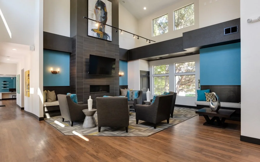 Modern living room with gray and blue accents, large windows, and a high ceiling.
