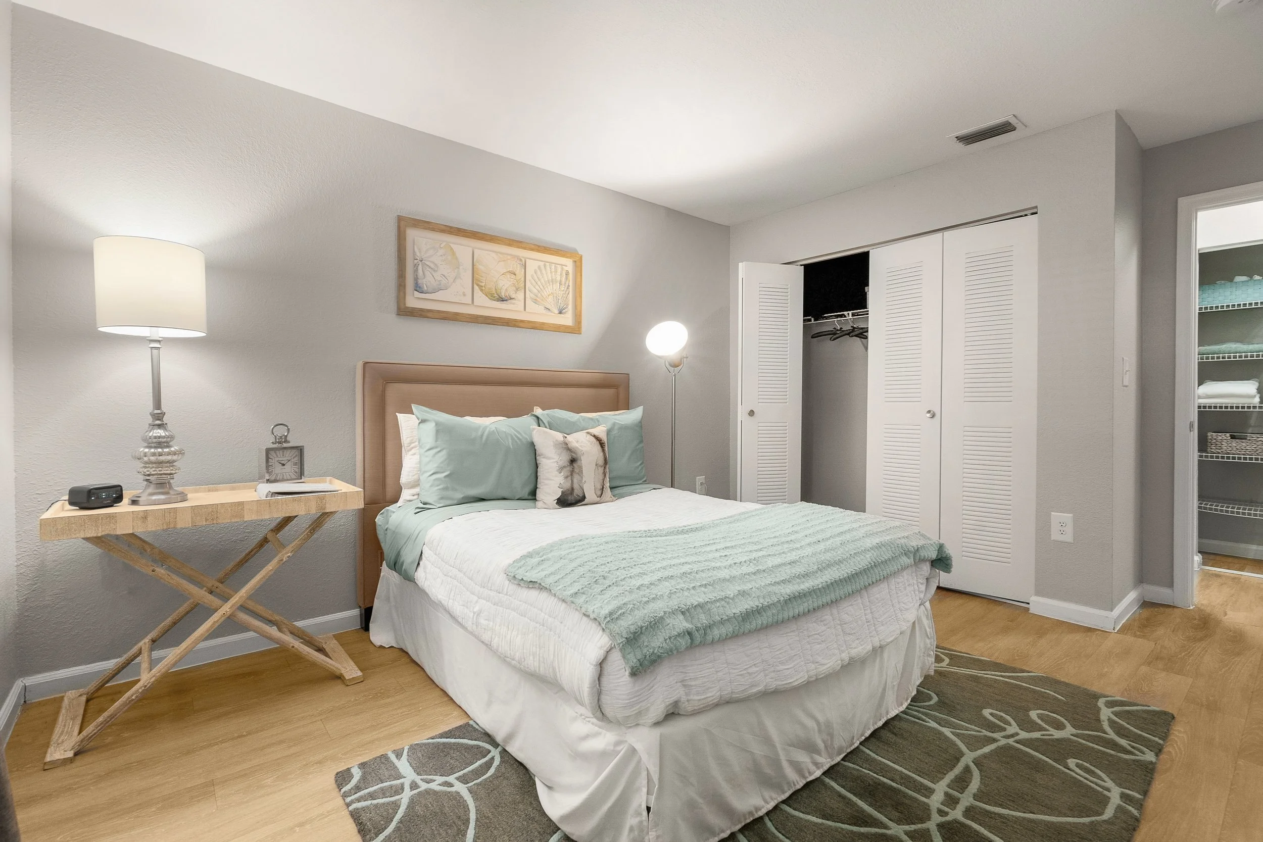 A bedroom with a bed, side table, lamp, and closet.