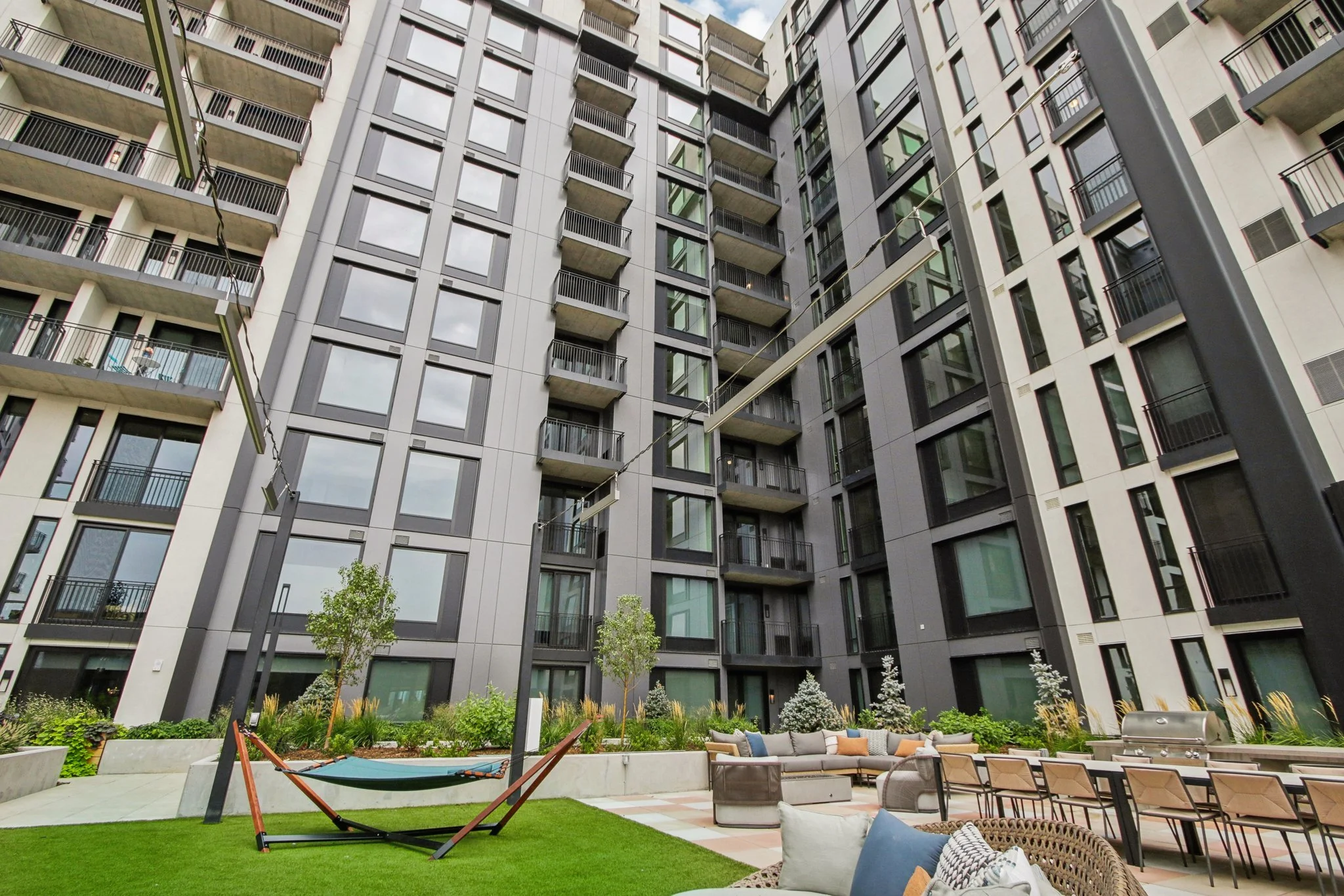 View of modern apartment building courtyard with outdoor seating, green plants, trees, and hammock.
