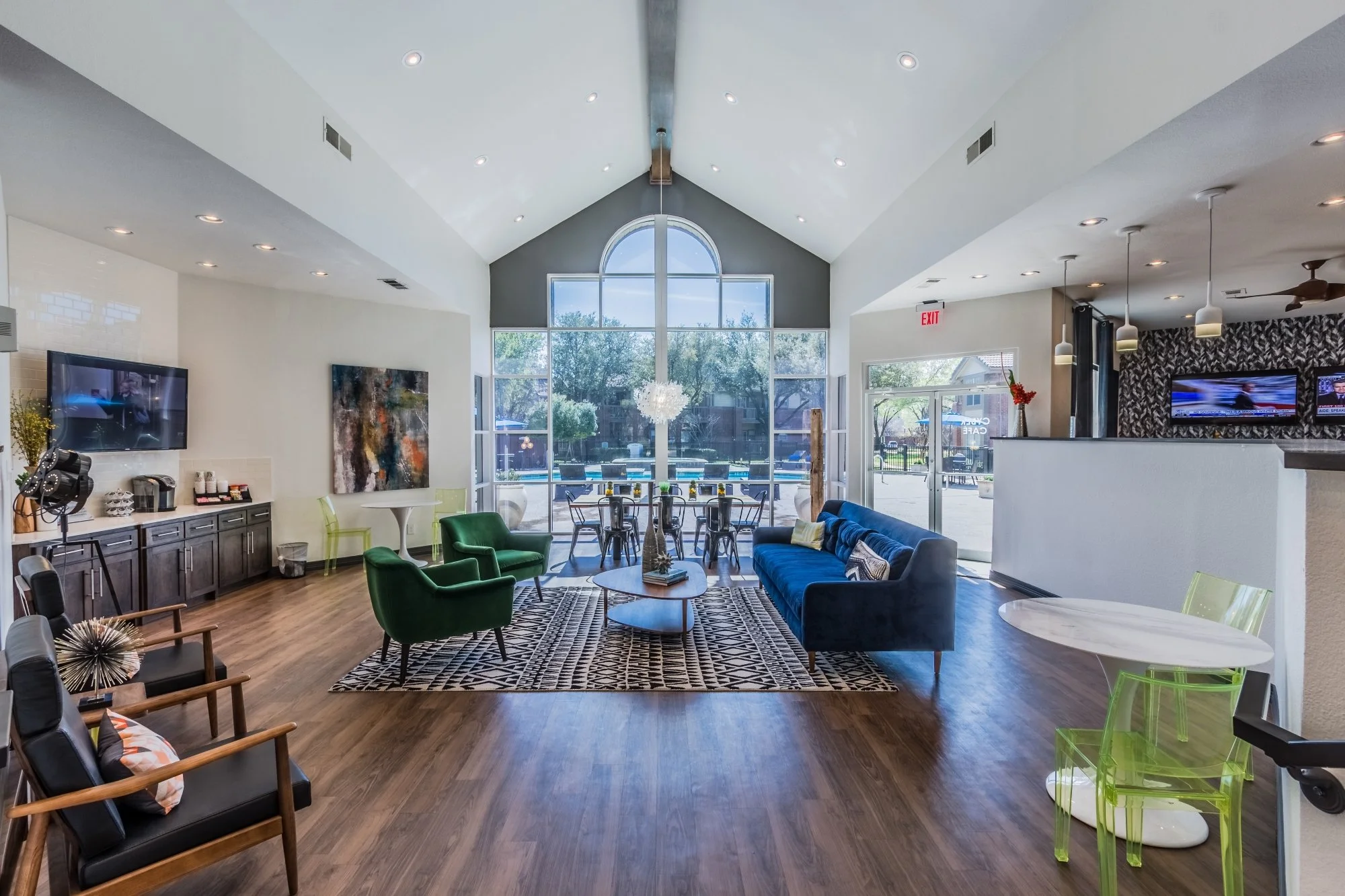 Modern interior of a community lounge with large floor-to-ceiling windows, colorful seating including green chairs and a blue sofa, and contemporary decor.