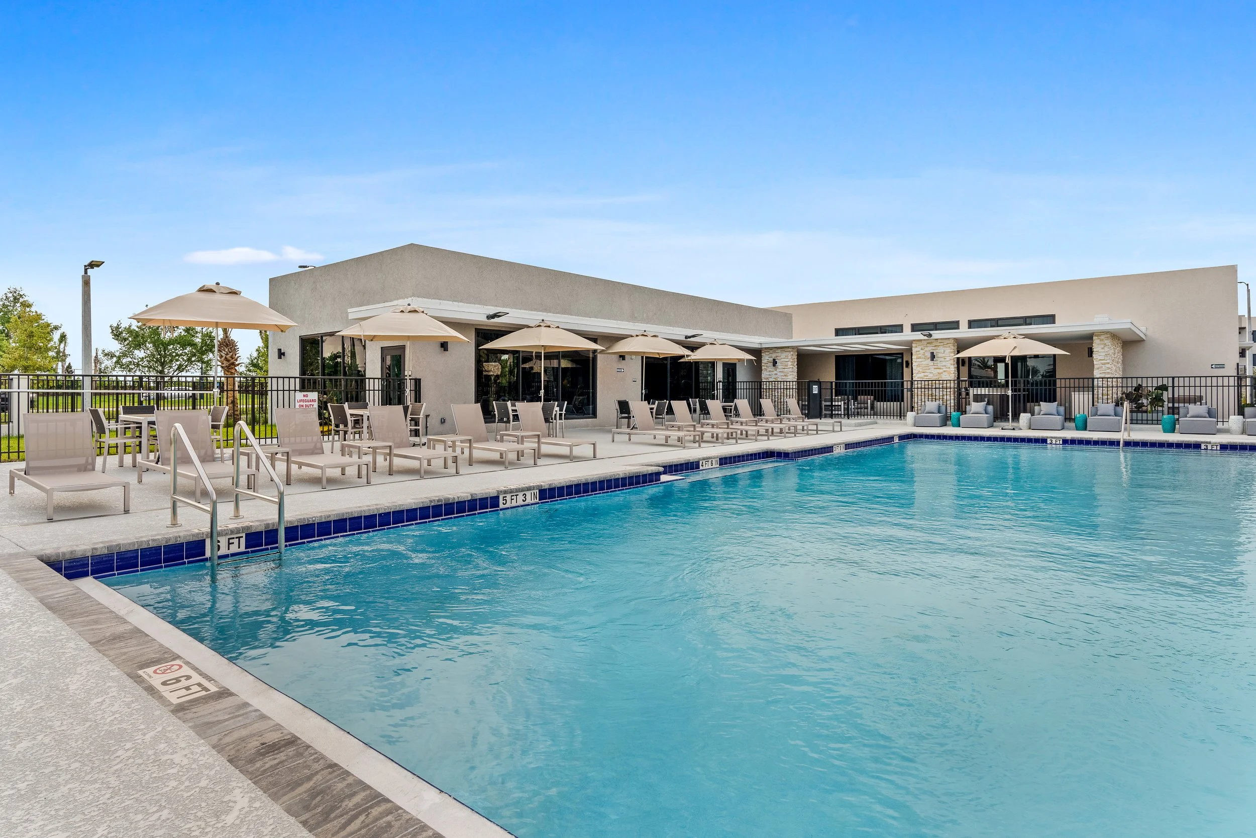Empty outdoor swimming pool with lounge chairs and umbrellas, modern building in the background, clear blue sky