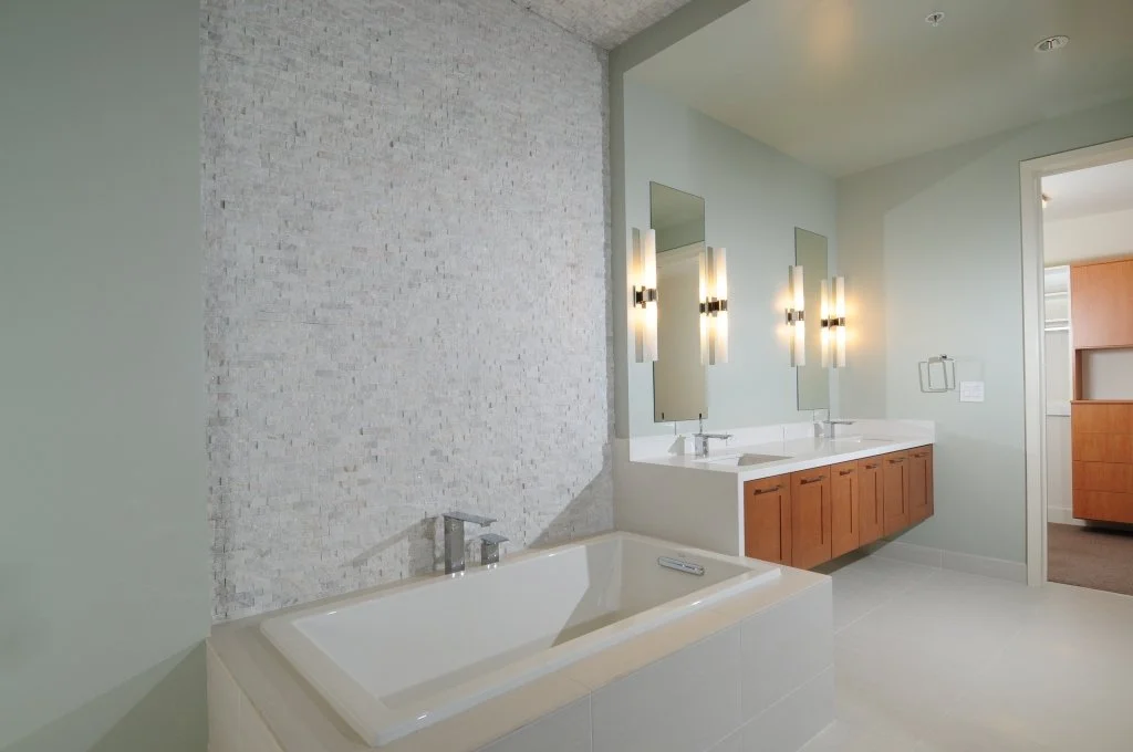 Modern bathroom with a white bathtub, double sink vanity with wooden cabinets, and illuminated mirrors.