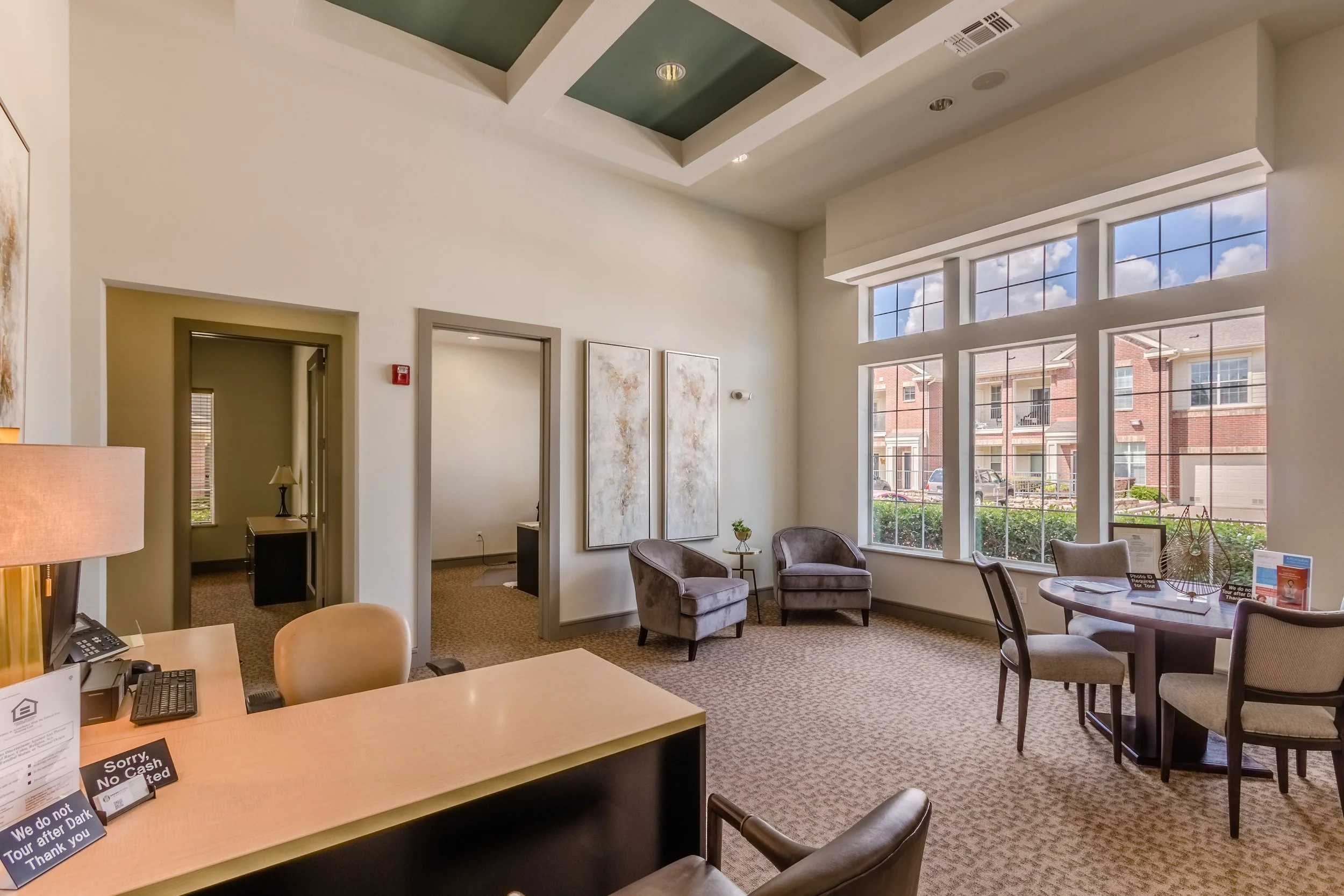 Interior of a modern apartment leasing office with large windows, a reception desk, chairs and tables, and artwork on the walls.