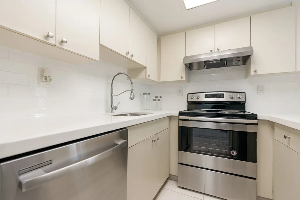 Kitchen with white cabinets, stainless steel oven, range hood, sink, and countertop.