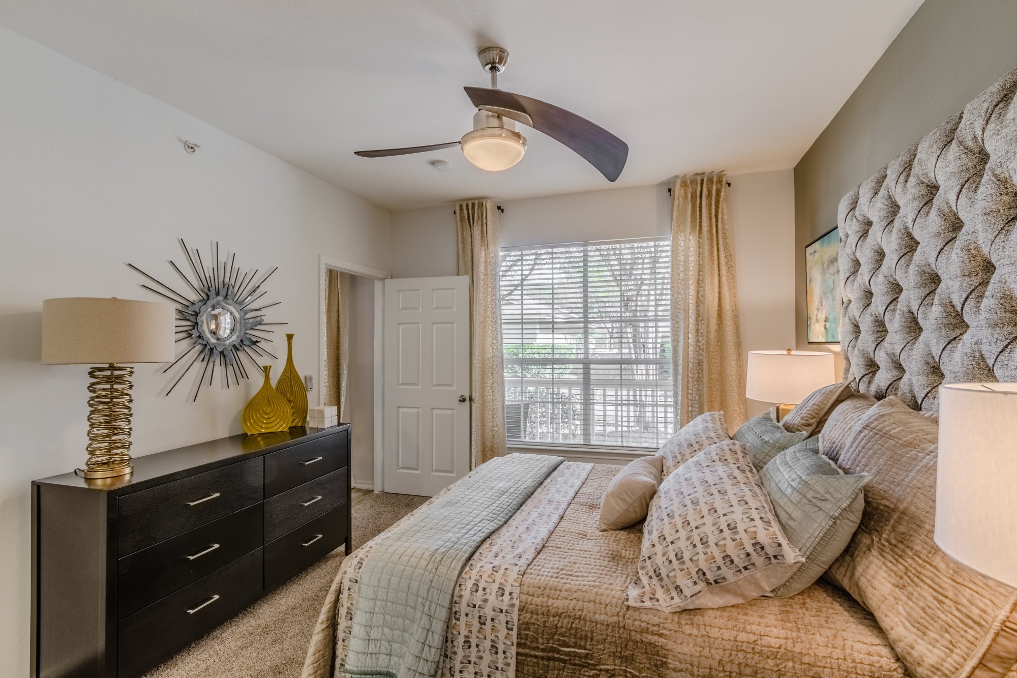 A bedroom with a bed, lamps, a dresser, and a window with blinds and curtains.