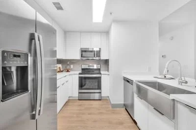 Modern kitchen with stainless steel refrigerator, microwave, oven, white cabinets, and a double sink on a white countertop.
