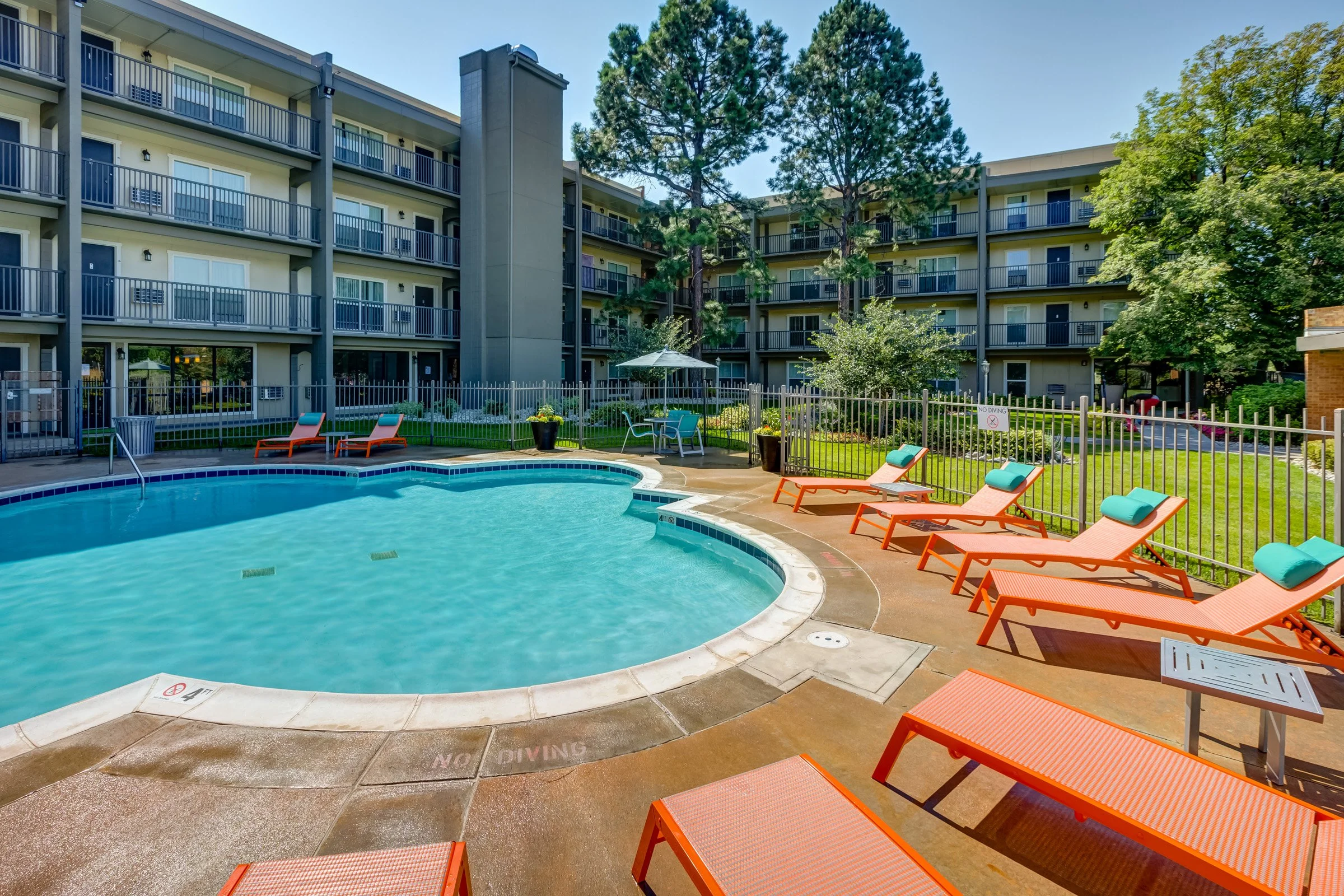 A residential apartment complex with a swimming pool and lounge chairs in the courtyard.