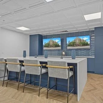 Conference room with a large white table, six white chairs, and two wall-mounted screens displaying a building.
