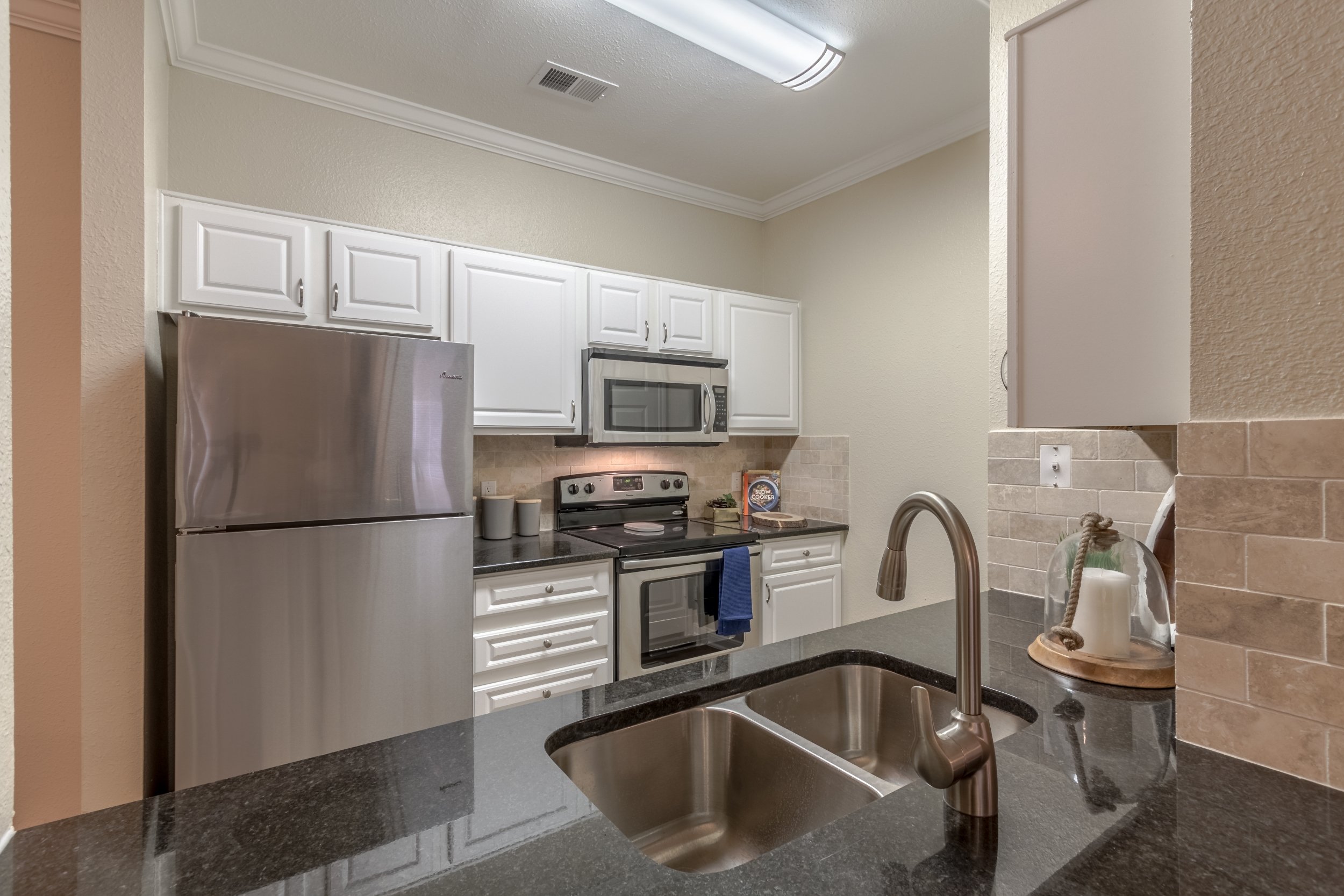 Kitchen with white cabinets, stainless steel refrigerator, microwave, and stove; black countertop with a sink and modern faucet.