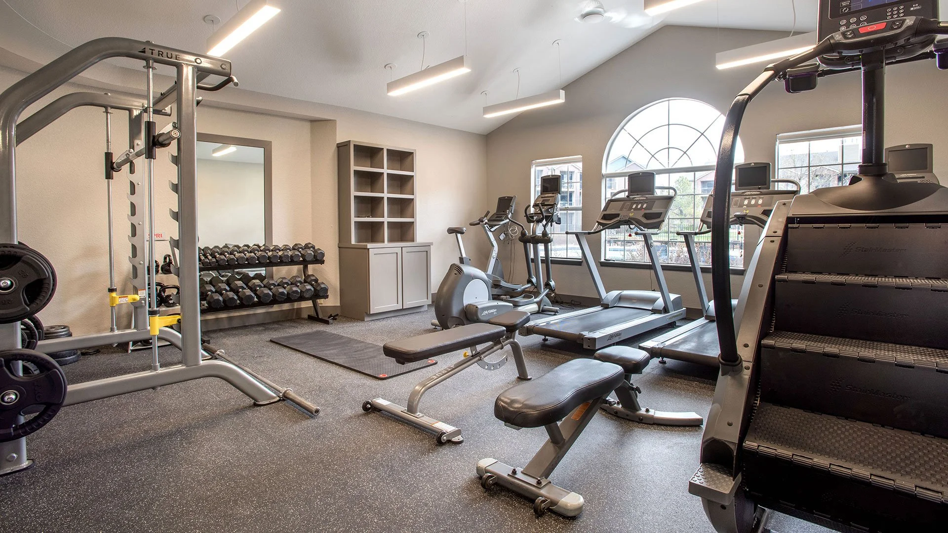 An indoor gym with treadmills, stationary bikes, warm-up equipment, and a rack of dumbbells.