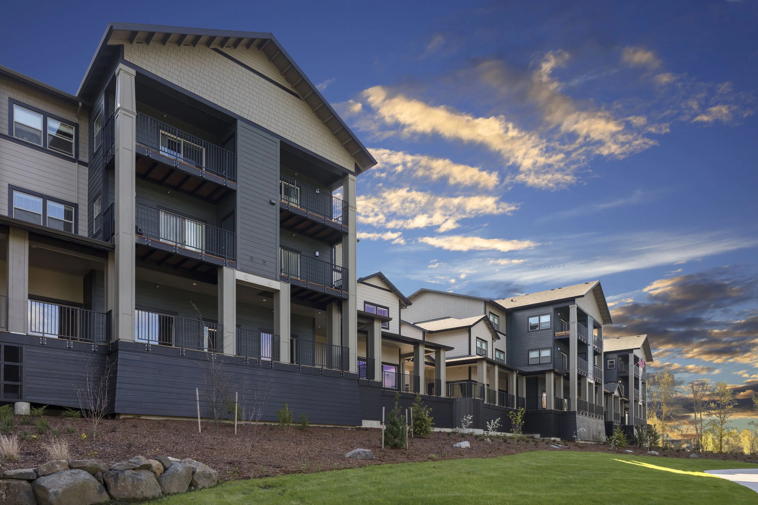 Exterior view of modern multi-story apartment complex during sunset with landscaped yard and sky with clouds.