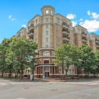 Multi-story residential building with trees in front, blue sky and clouds overhead.