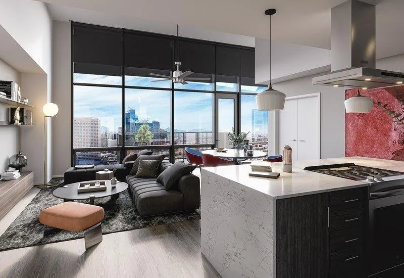 Modern living room with large windows showing city skyline, black sofa, round coffee table, and a kitchen island with books and decor items.