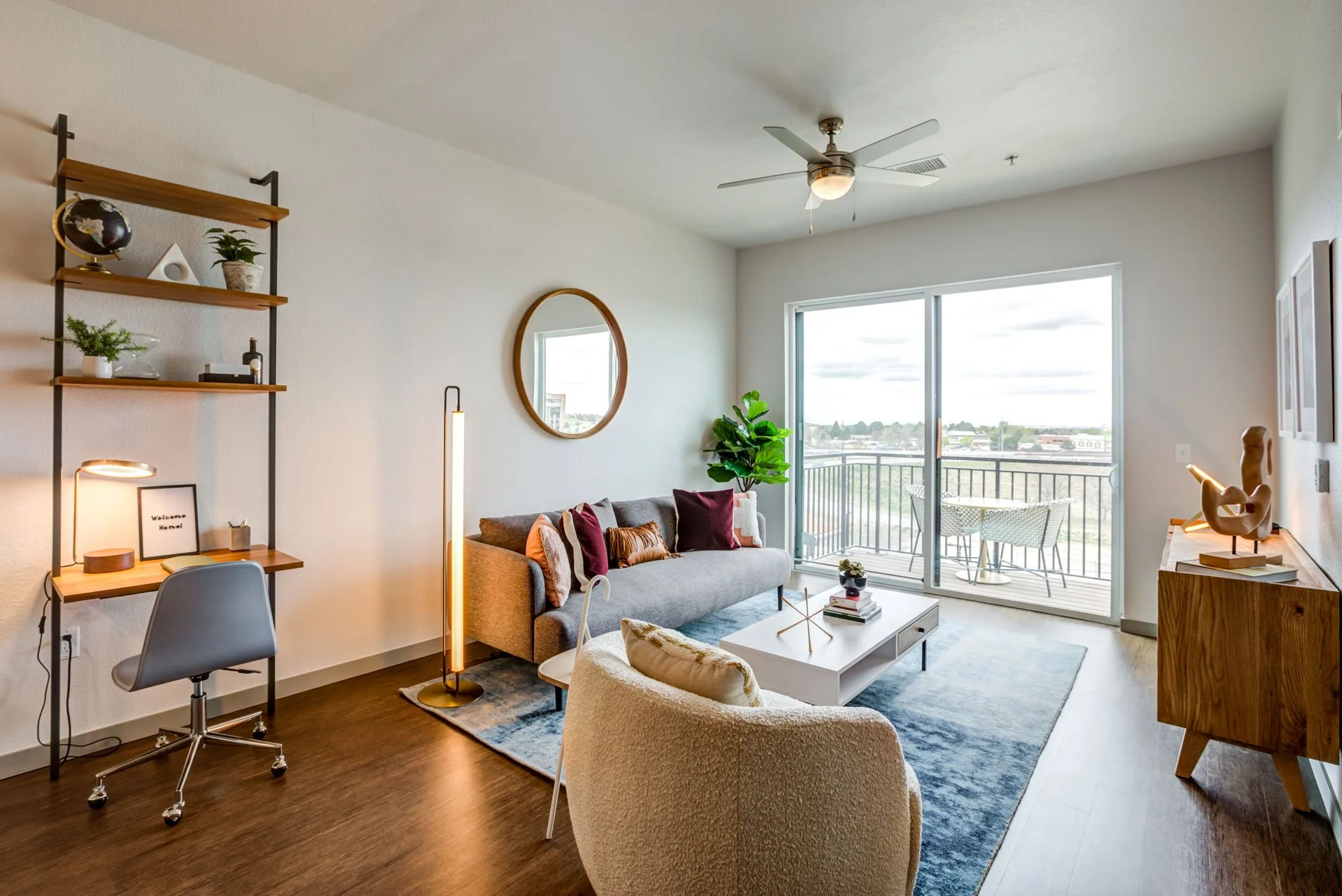 Modern living room with gray sofa, white armchair, wooden sideboard, bookshelf, and sliding glass door to balcony.