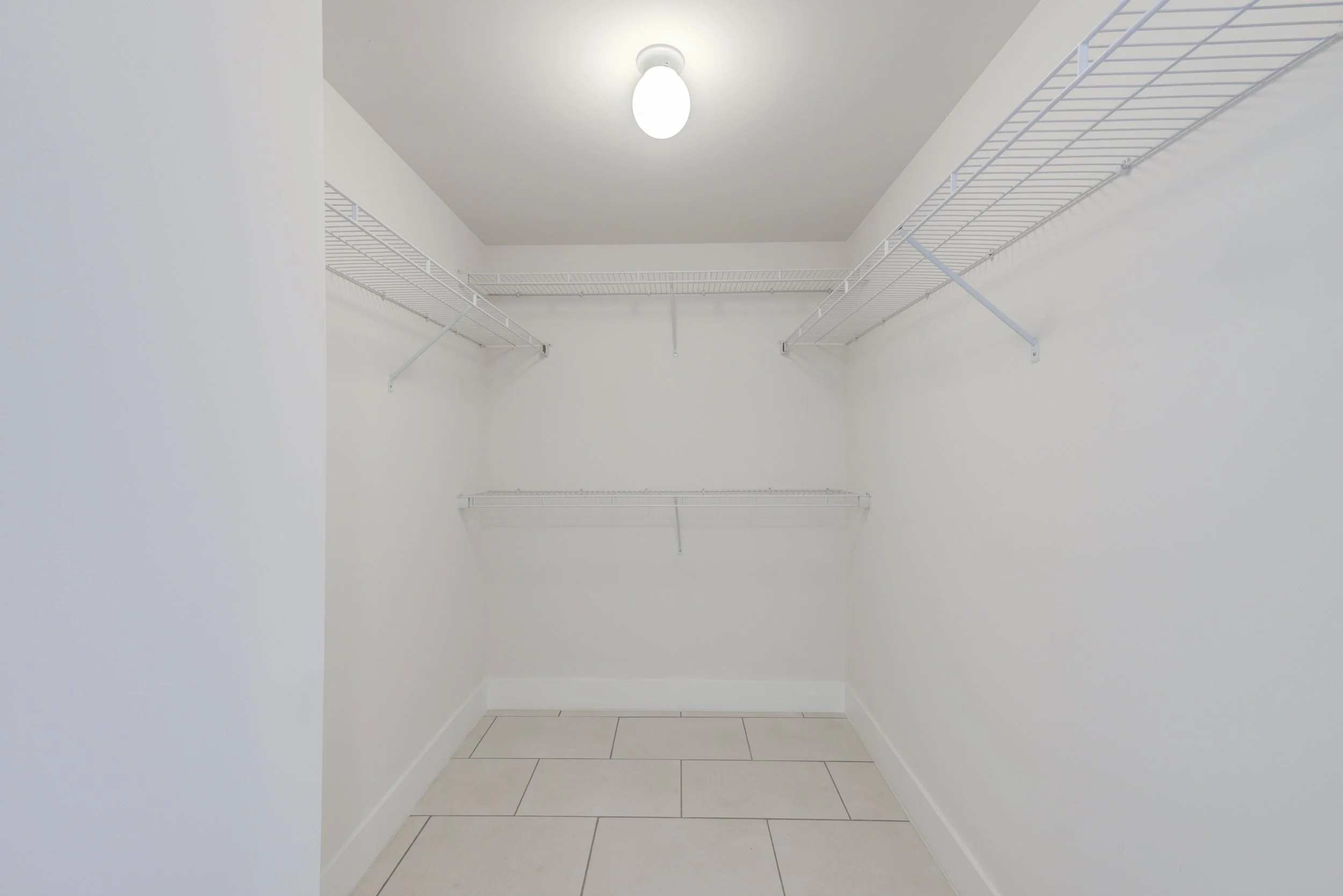 Empty white walk-in closet with wire shelving on three walls, illuminated by ceiling light.