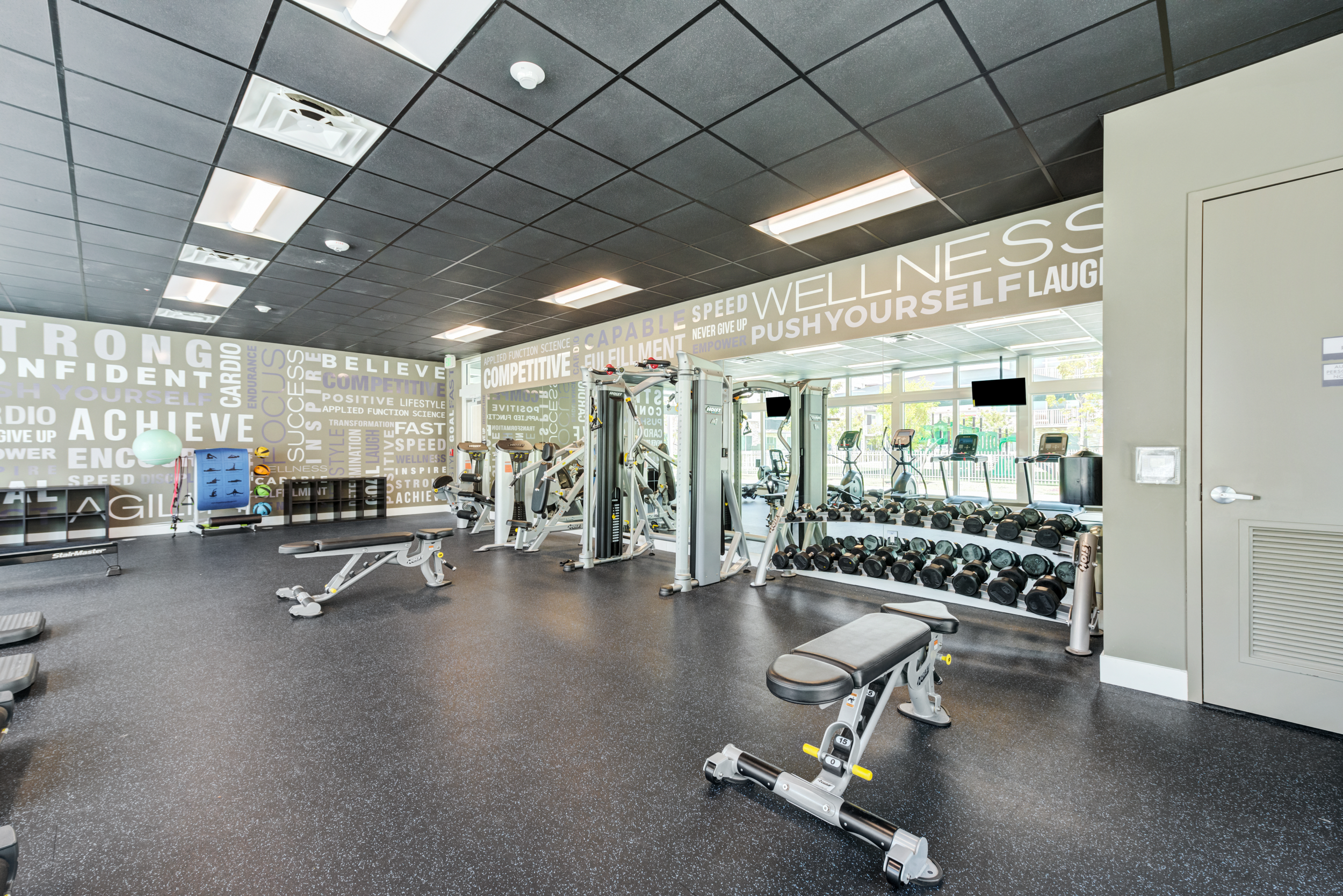 Empty gym room with workout equipment, weights, and motivational words on the wall.