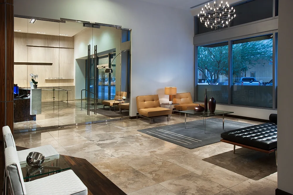 Modern hotel lobby with beige seating, glass coffee tables, large windows, and a chandelier.