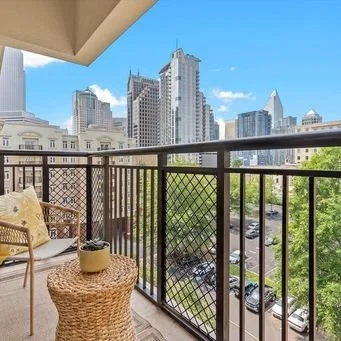 Balcony with wicker table and chair, overlooking a city skyline with tall buildings and blue sky.