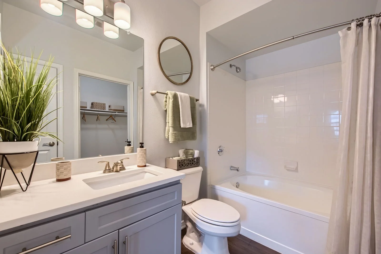 Bathroom with a vanity, mirror, toilet, bathtub with shower curtain, and decor including a potted plant and towels.