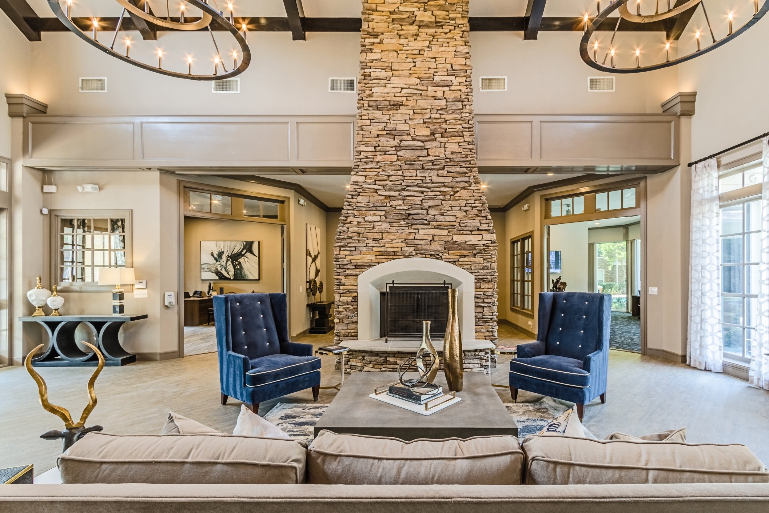 Living room with a large stone fireplace, two navy blue armchairs, a beige sofa, and modern decorations.