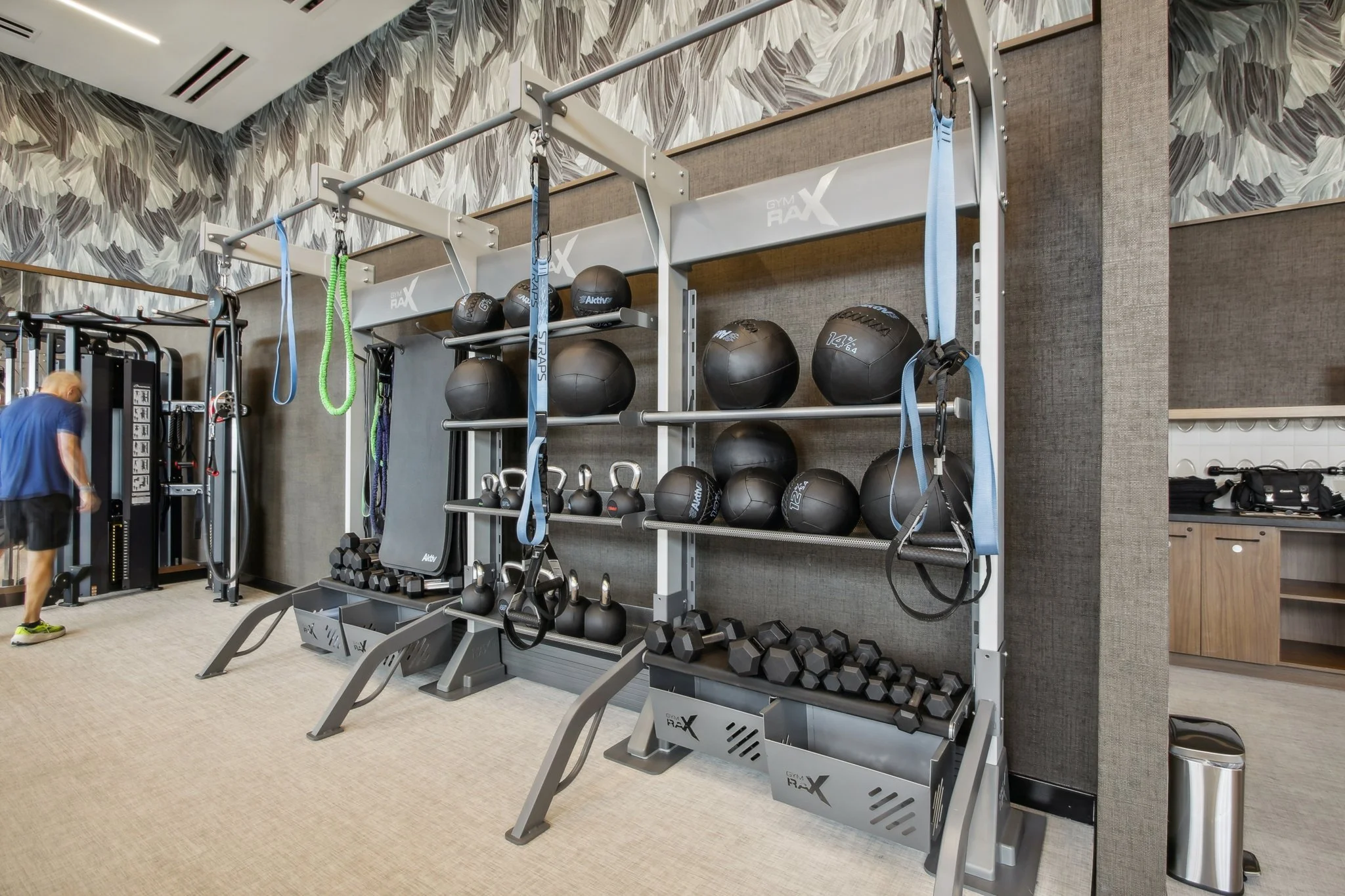Gym equipment rack with medicine balls, kettlebells, dumbbells, and resistance bands in a fitness center.