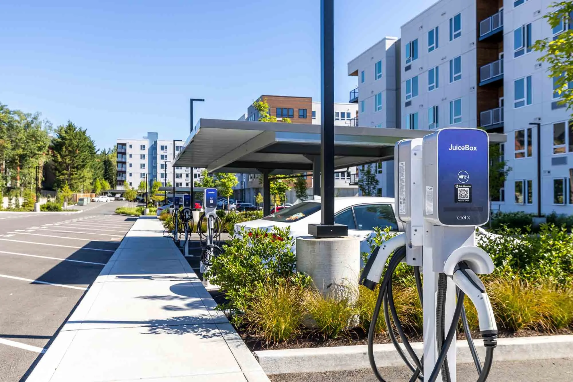 Electric vehicle charging station in a modern residential parking lot with apartment buildings in the background.