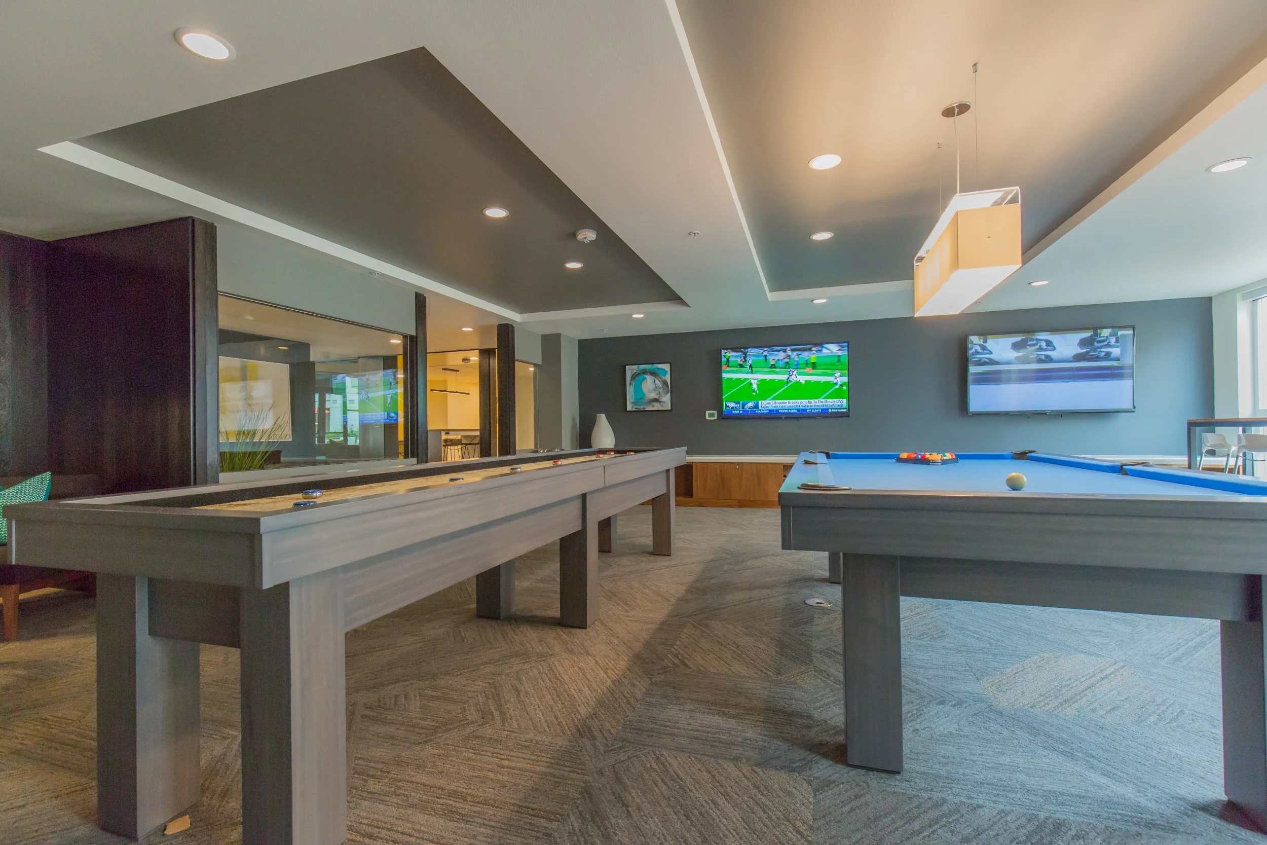 Indoor game room with pool tables and two wall-mounted TVs showing sports games.