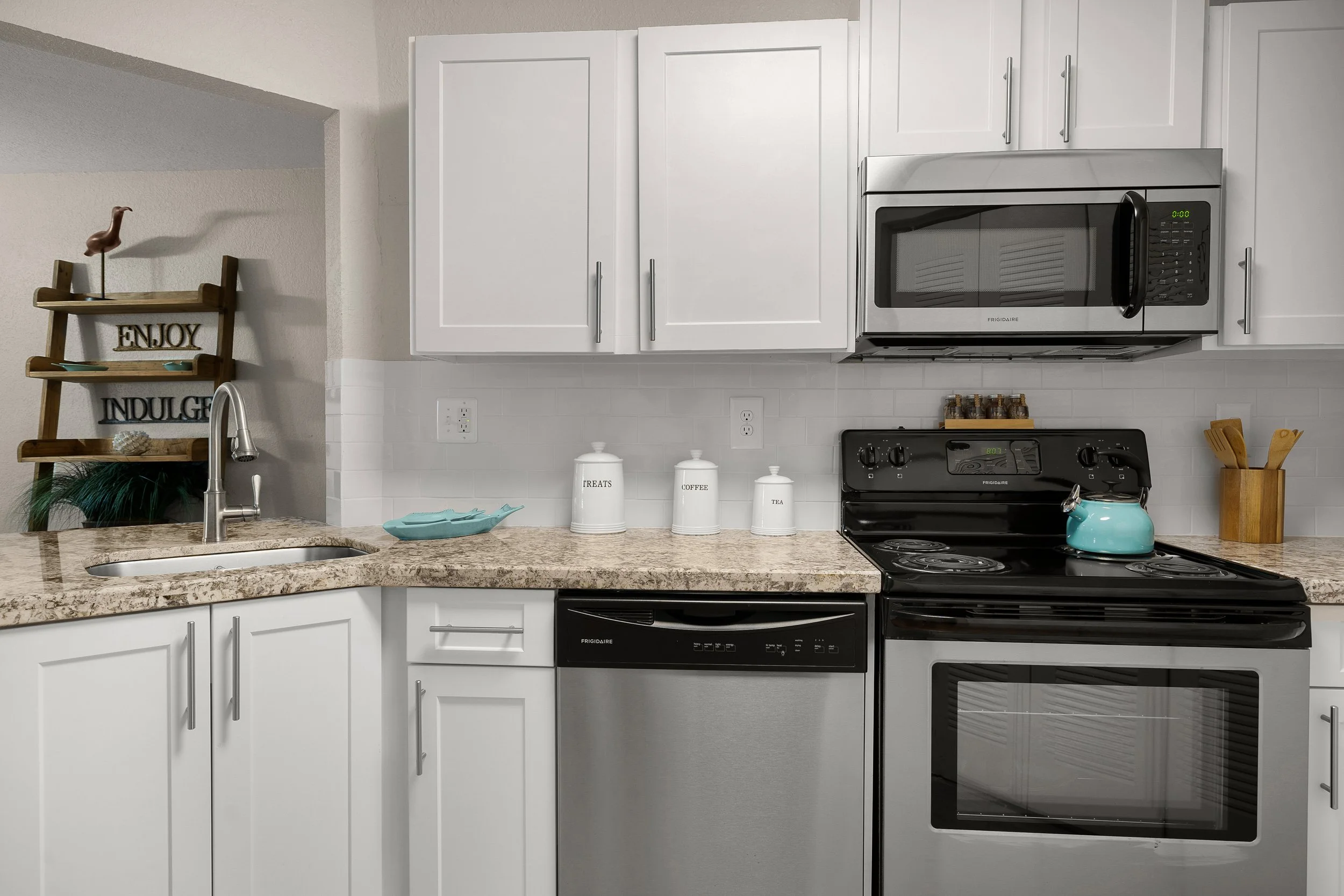 Kitchen with white cabinets, a granite countertop, stainless steel microwave, dishwasher, and oven, and decorative jars labeled 'Treats,' 'Coffee,' and 'Tea' on the counter.